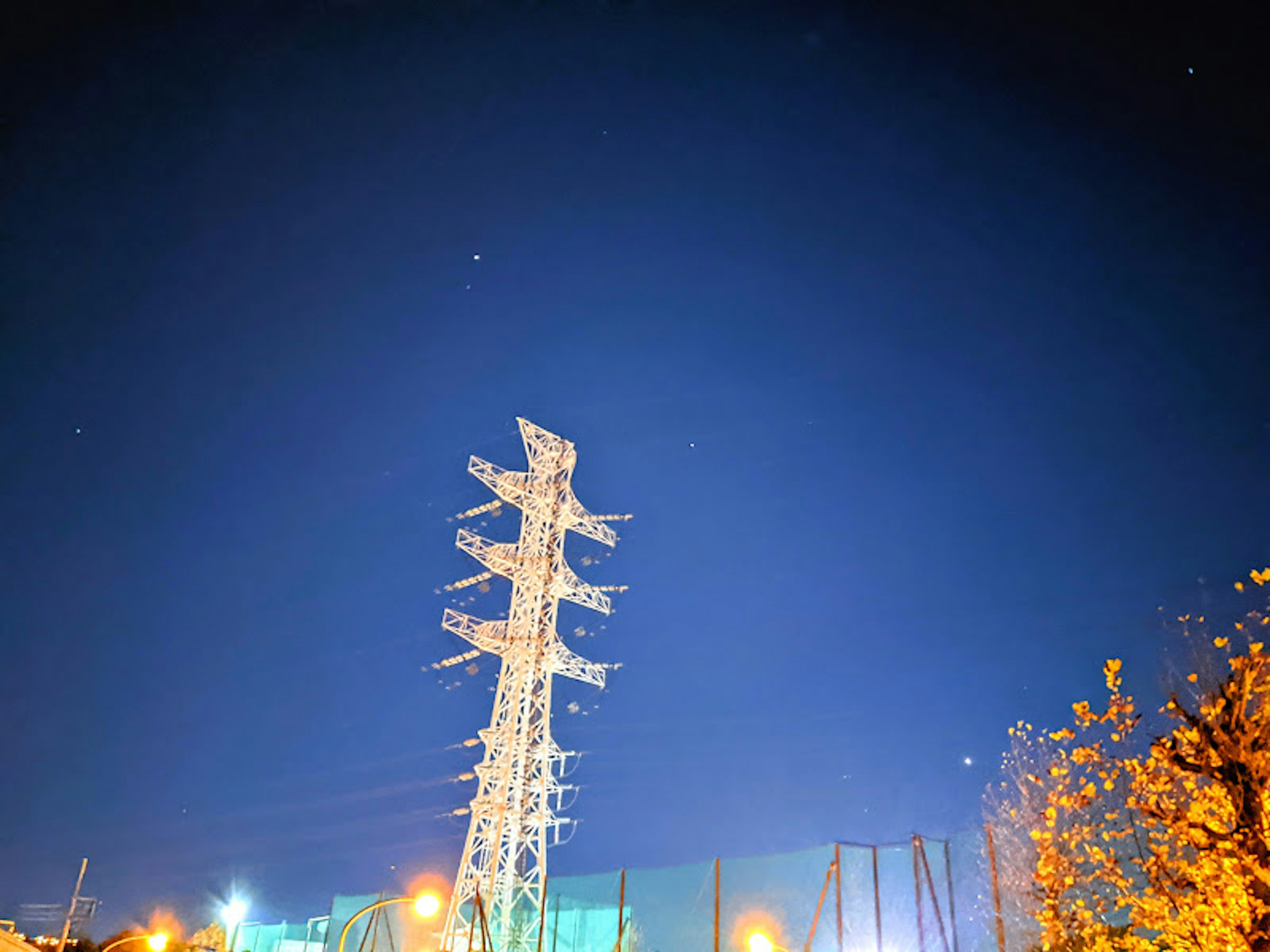 A tall power tower against a night sky with surrounding lights