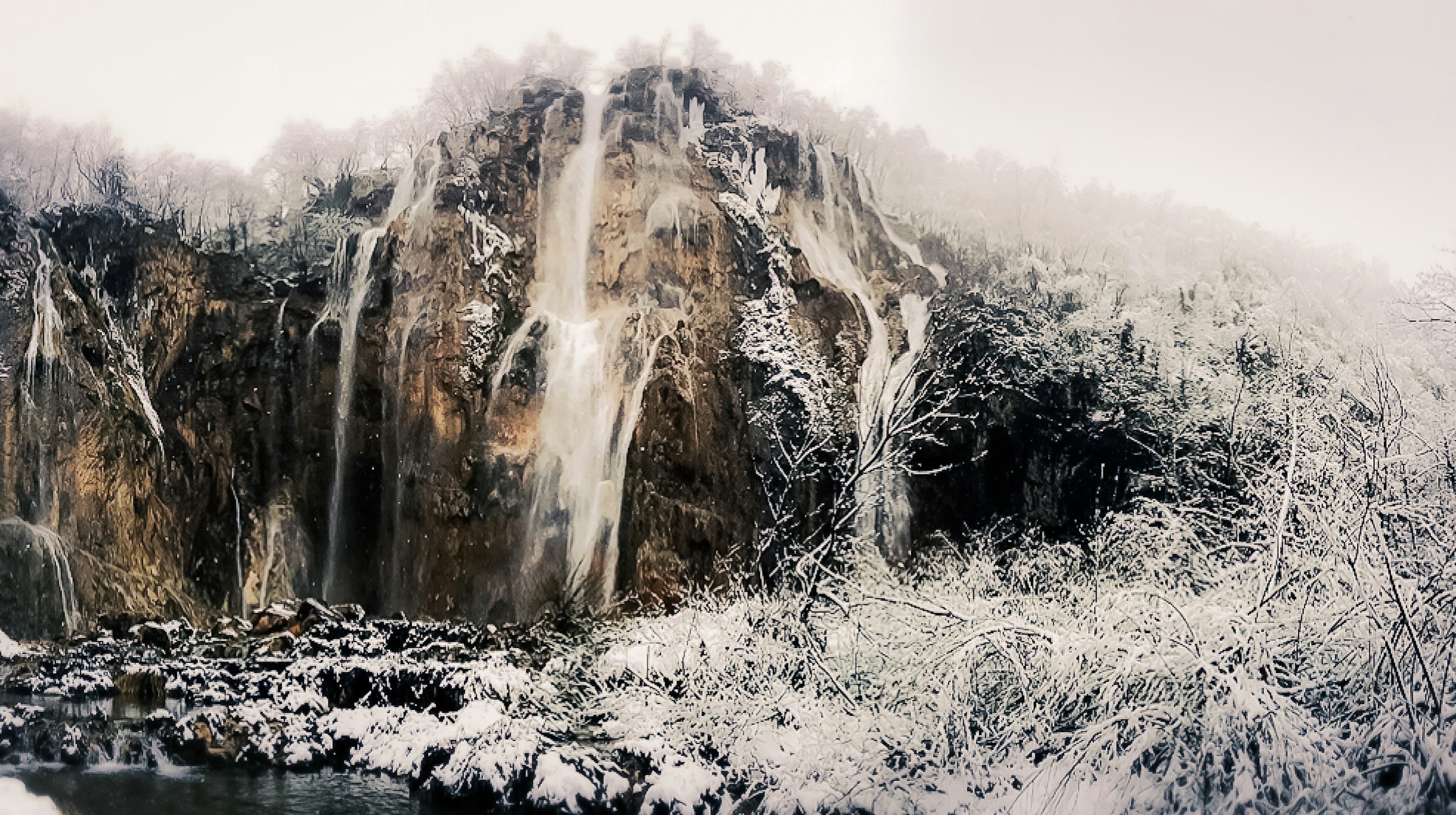 Air terjun yang tertutup salju mengalir di tebing berbatu