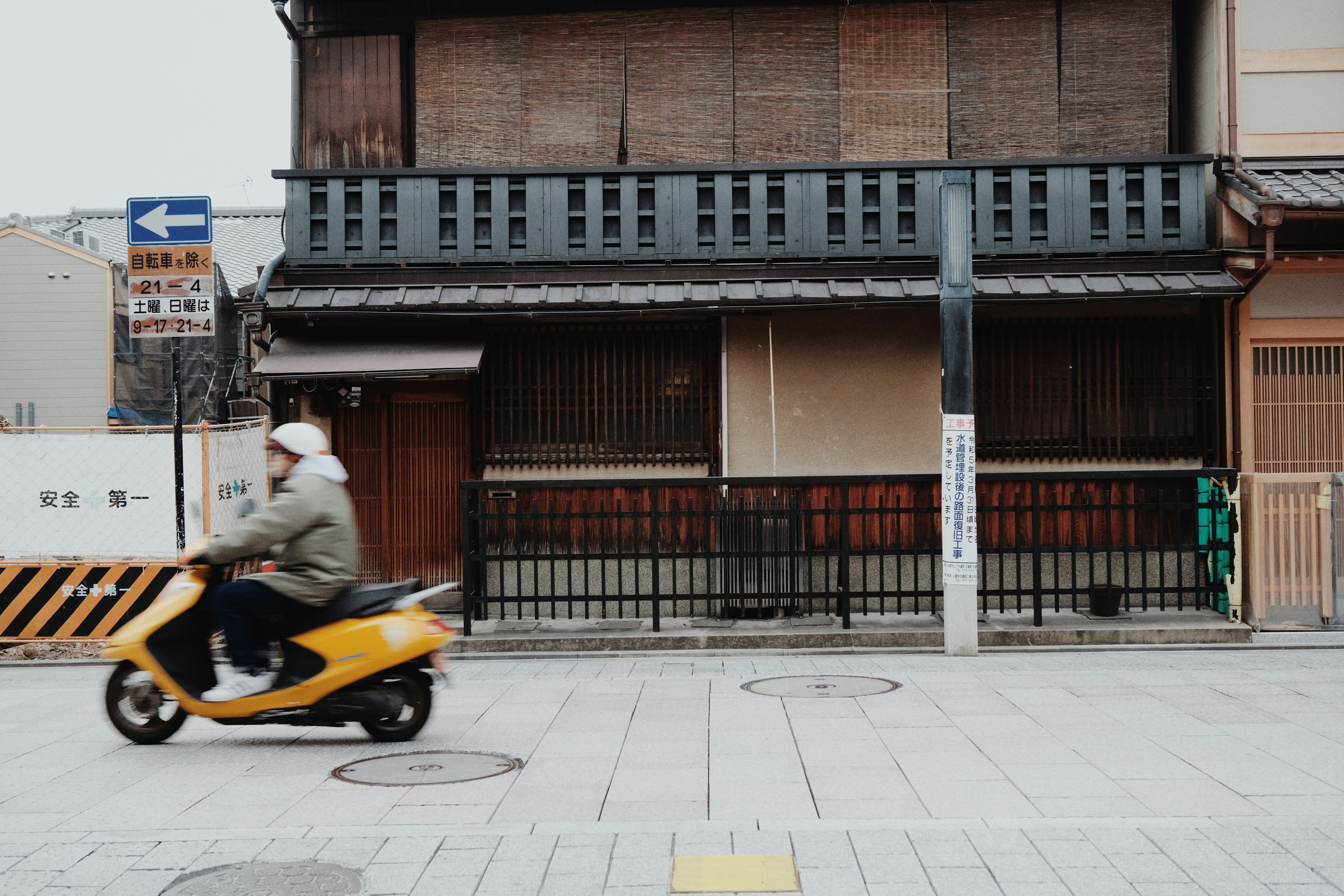 Una scooter amarilla pasando frente a una antigua casa japonesa