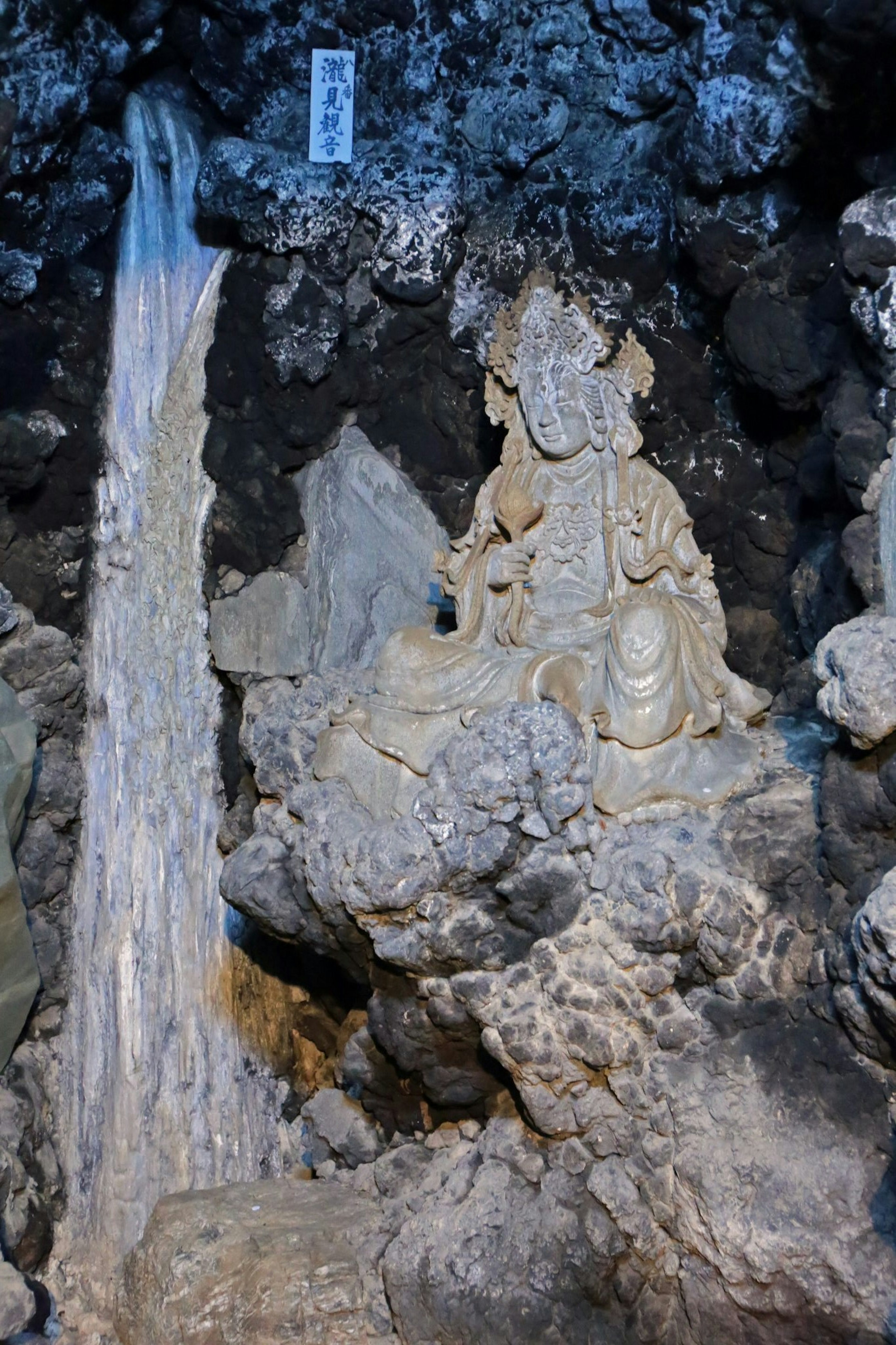 Carved statue of a deity in a rocky setting with flowing water