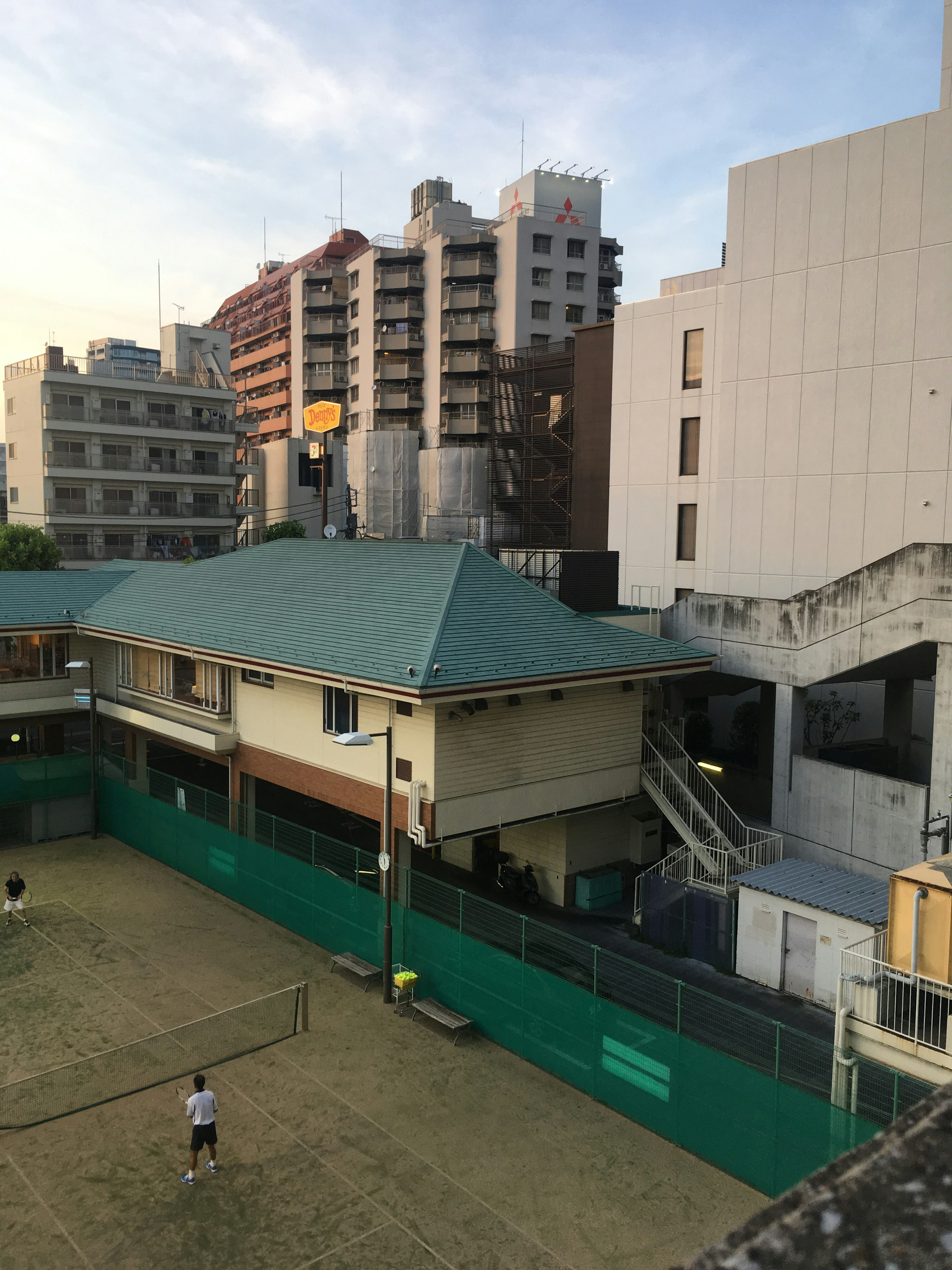 Evening view of a tennis court with surrounding buildings