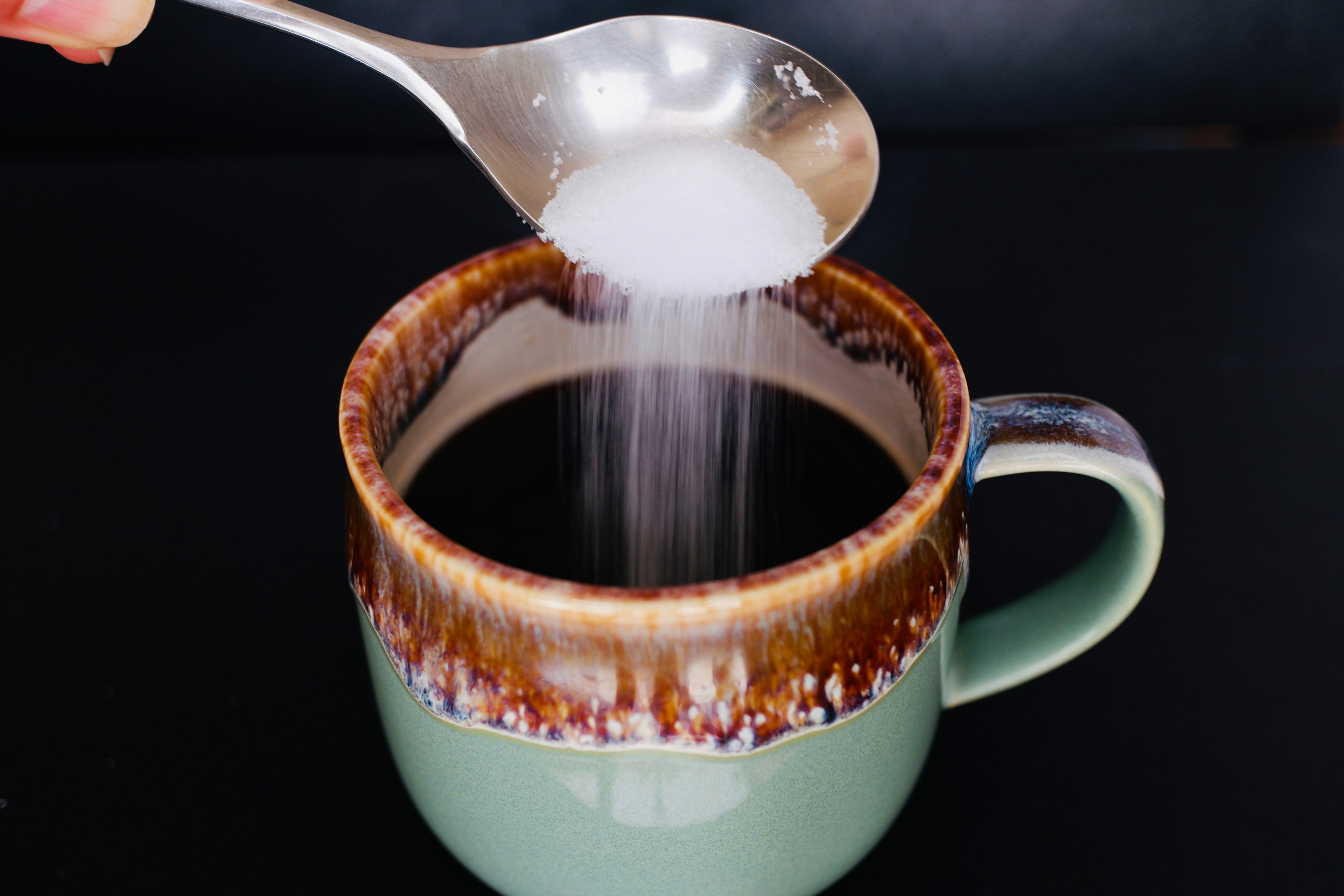 Image montrant du sucre ajouté au café une cuillère versant du sucre blanc dans une tasse