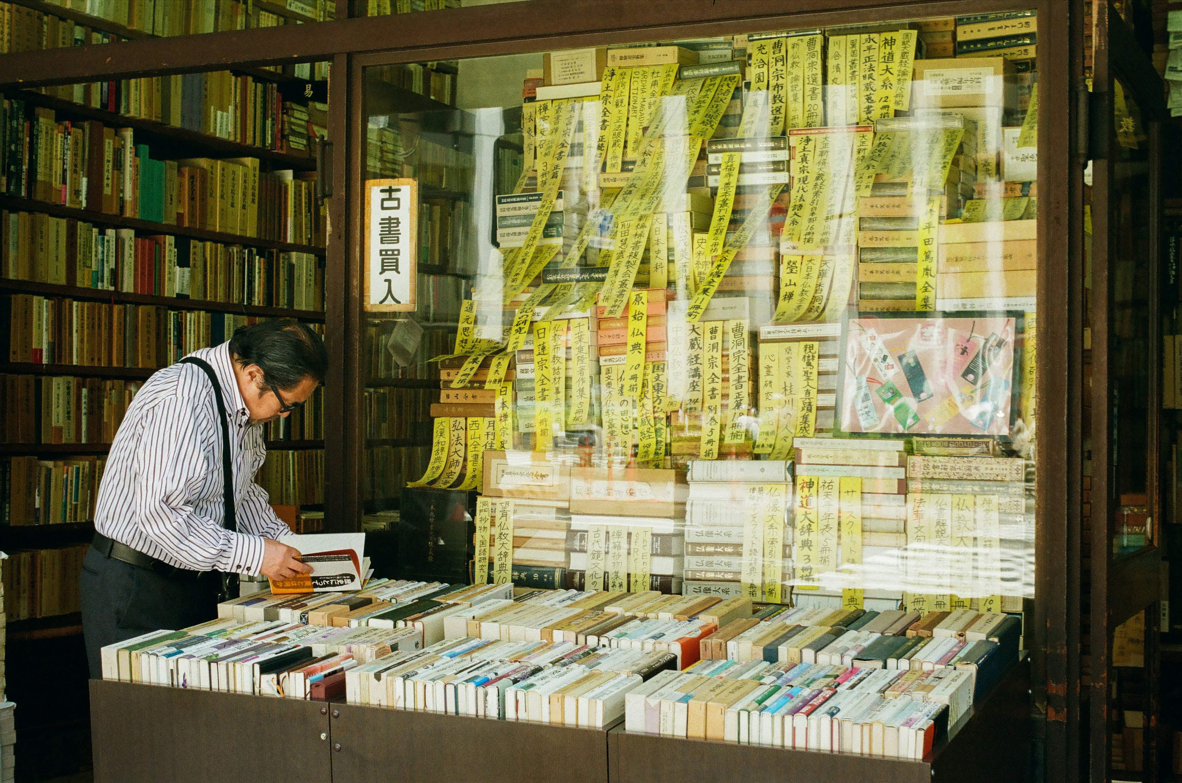 Ein Mann, der in einer Gebrauchtbuchhandlung Bücher durchblättert, mit zahlreichen Büchern zur Schau