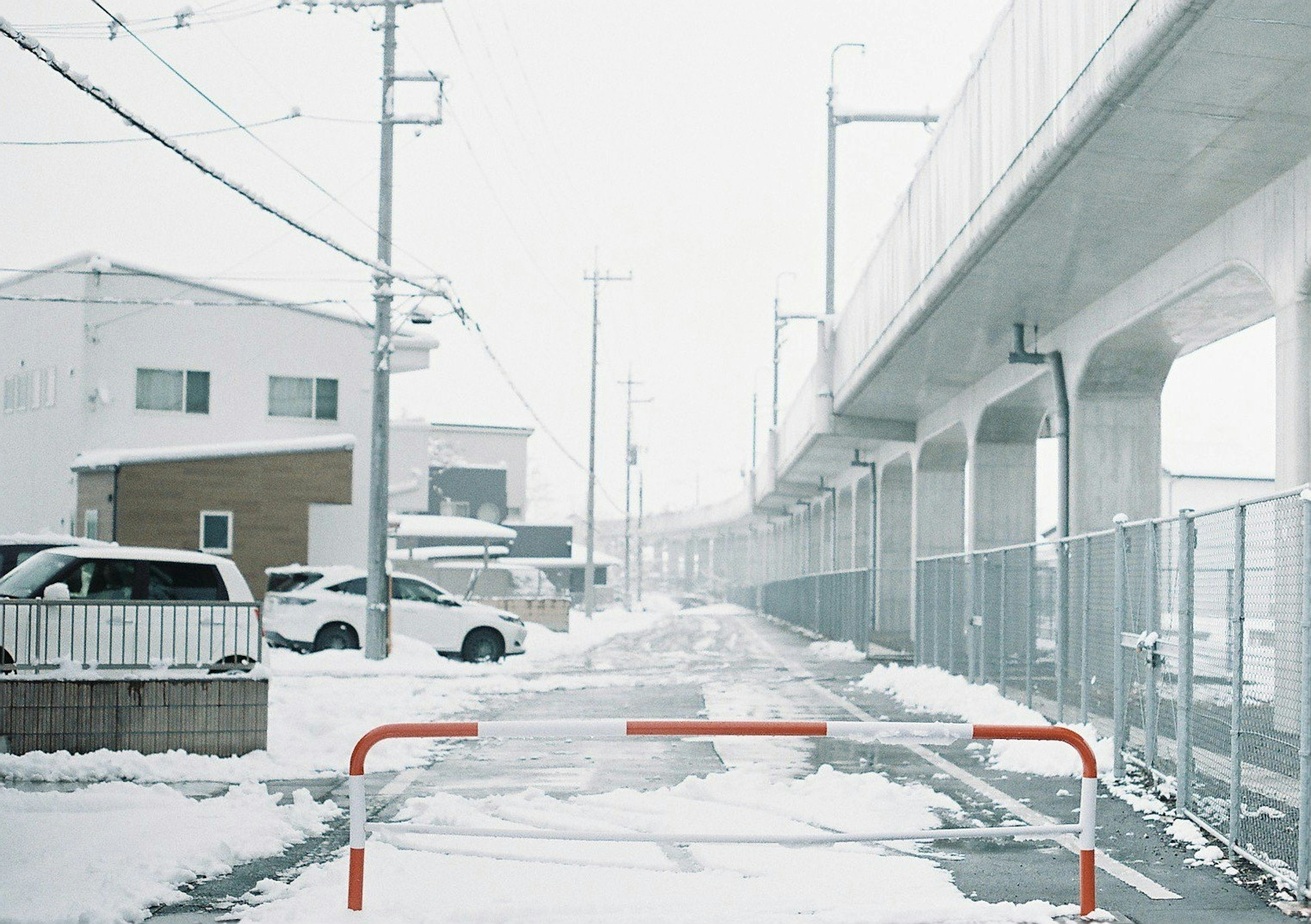 Schneebedeckte Straße mit einem Zugviadukt und geparkten Autos