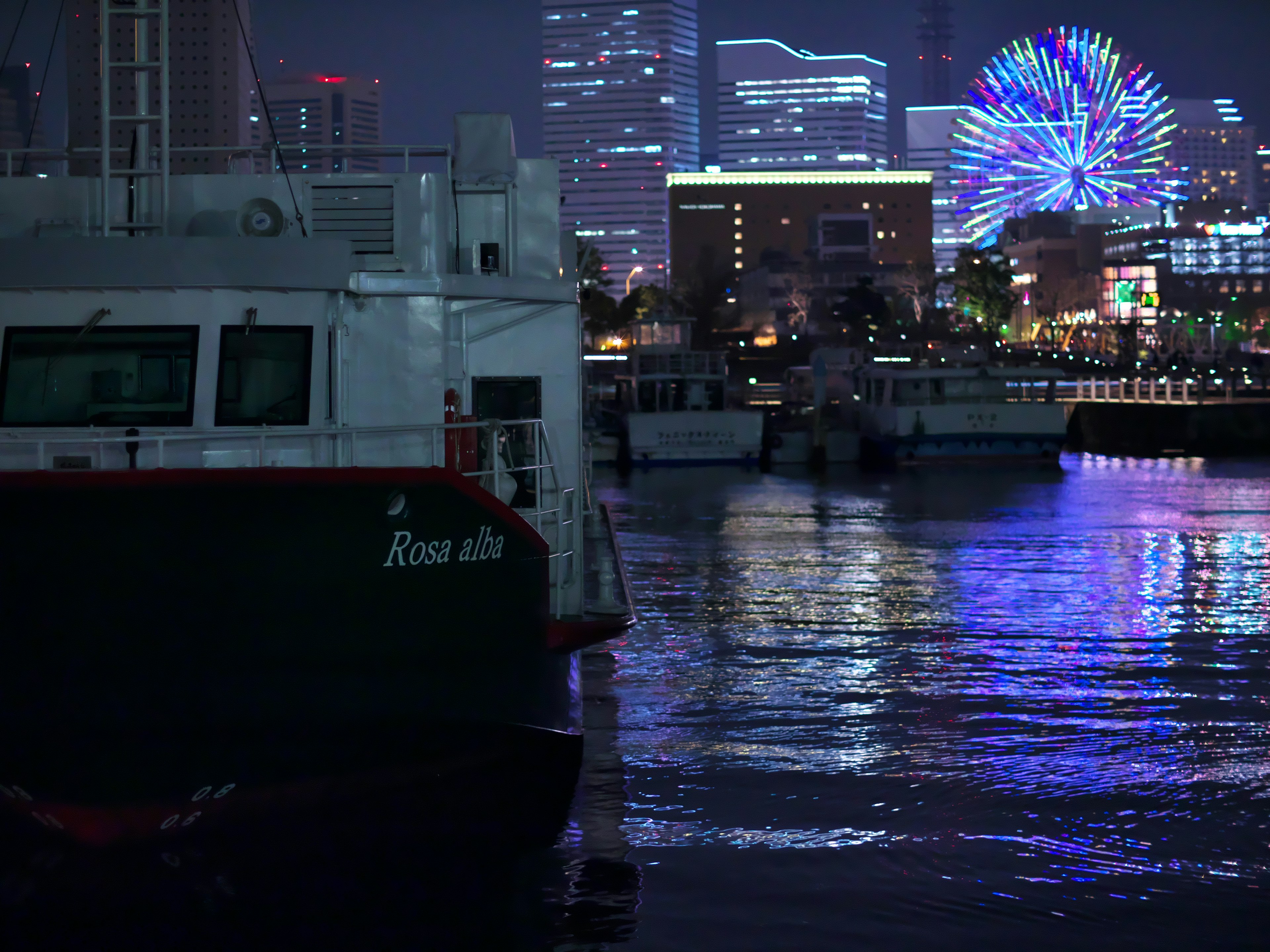 Boot im Hafen mit einem bunten Riesenrad im Hintergrund bei Nacht