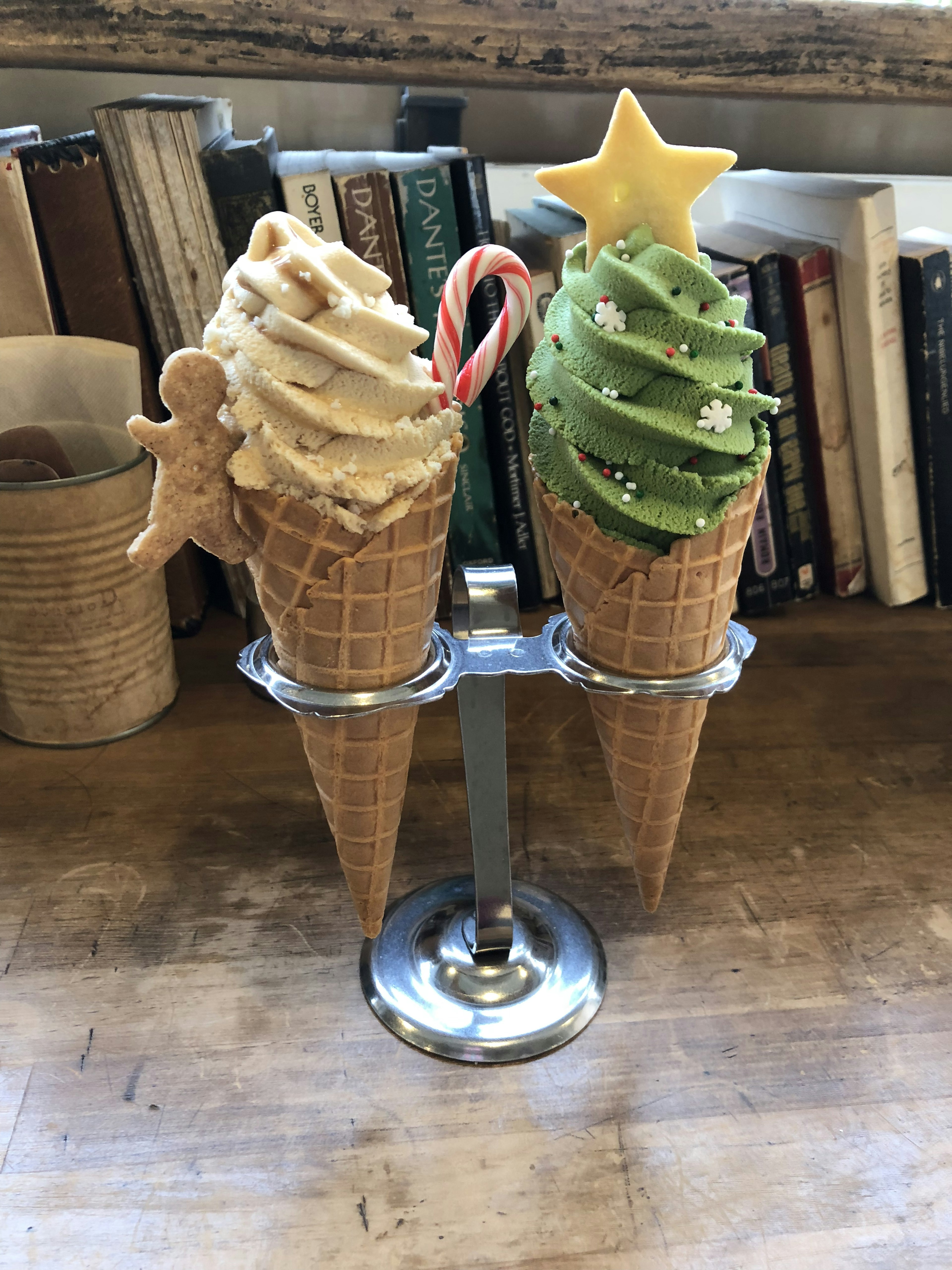 Two ice cream cones displayed in a holder one topped with cookie decoration and the other with green swirl and star decoration