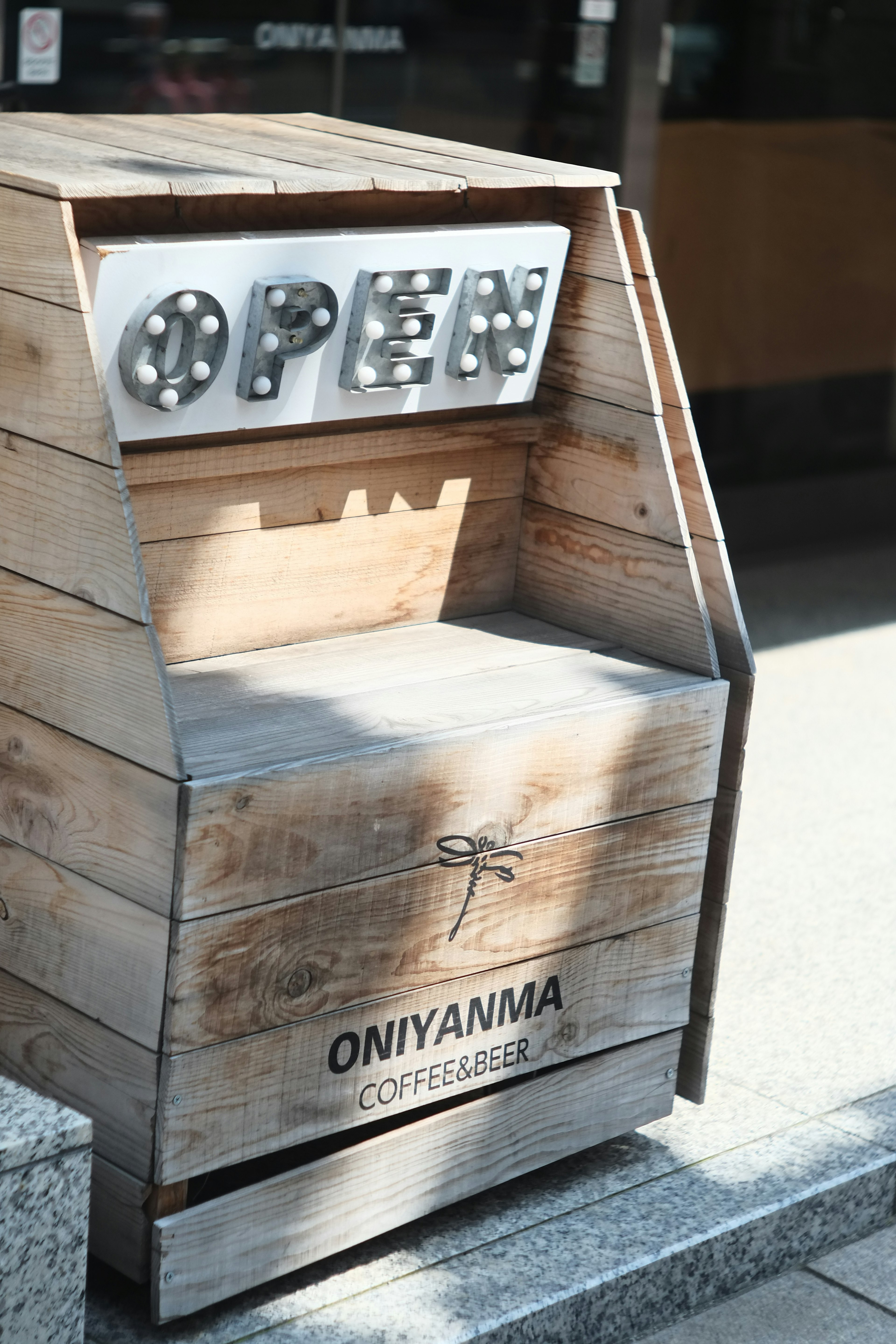 Wooden sign with bright bulbs spelling OPEN