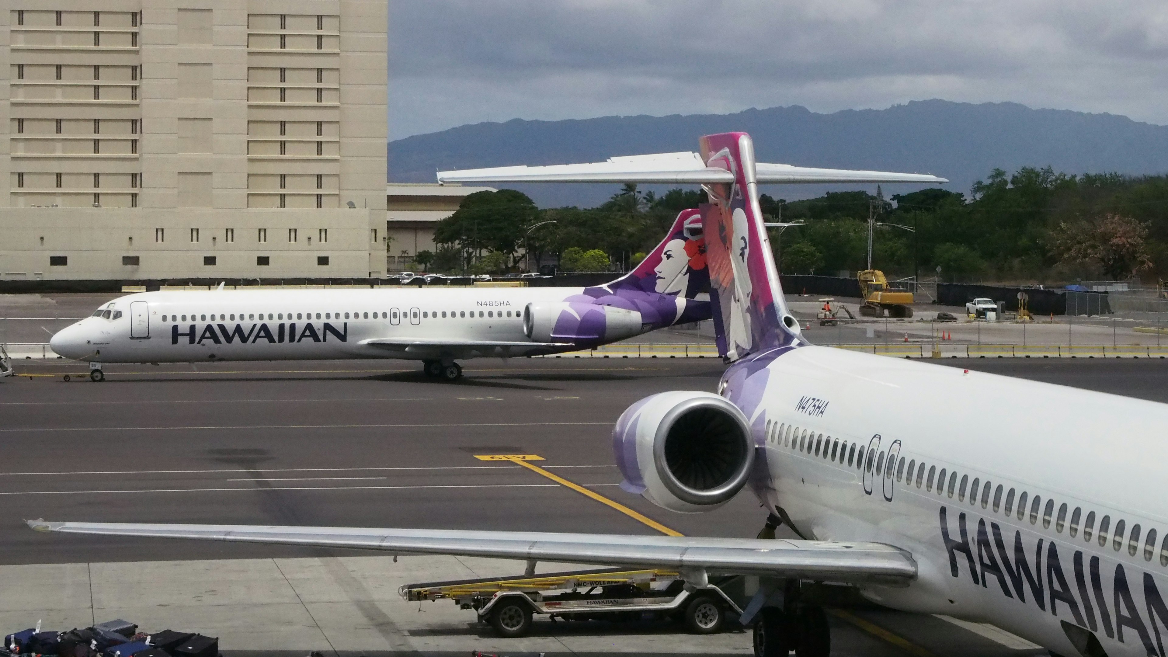 Two Hawaiian Airlines planes at the airport with mountains in the background