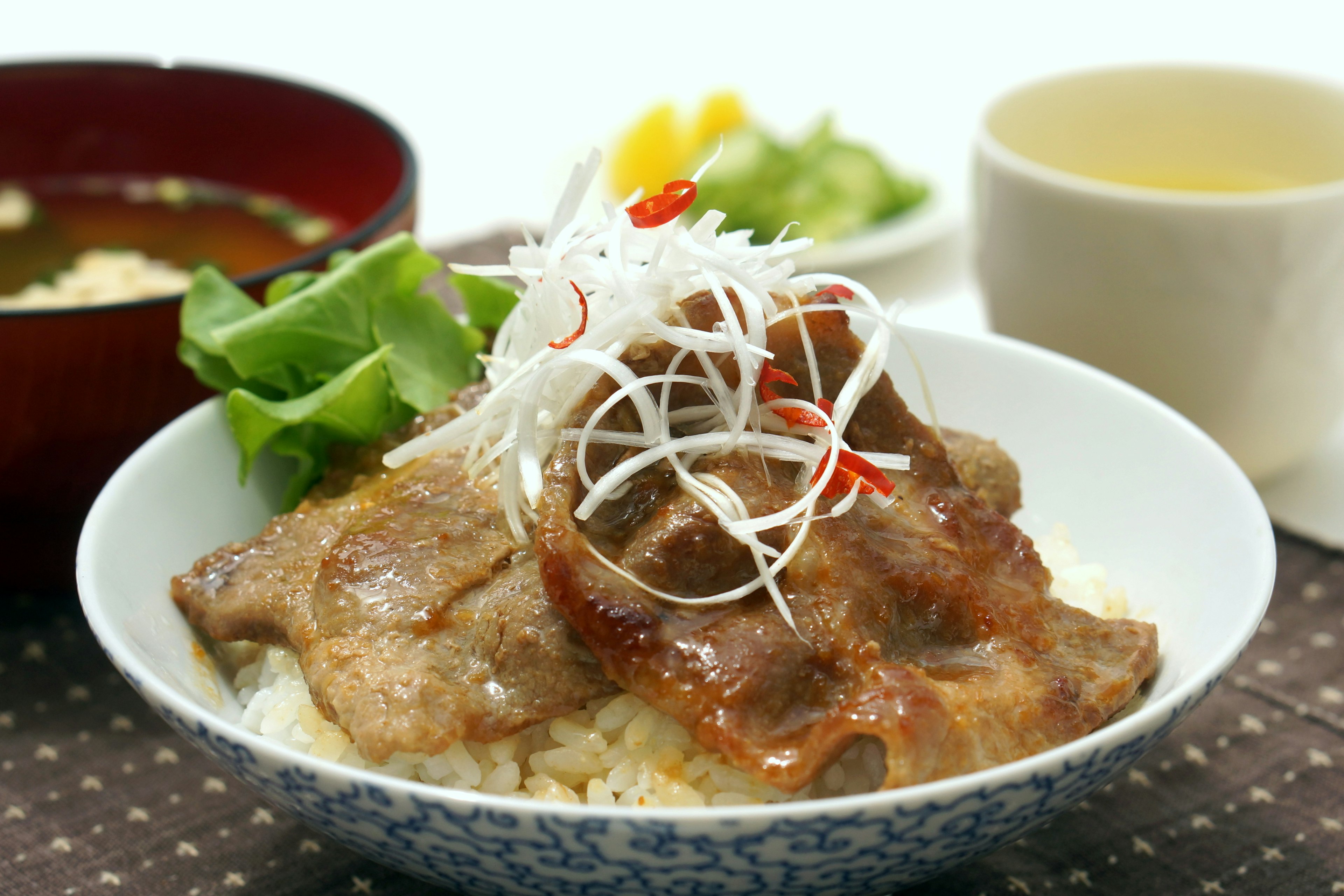 A rice bowl topped with grilled pork garnished with white onion and red chili