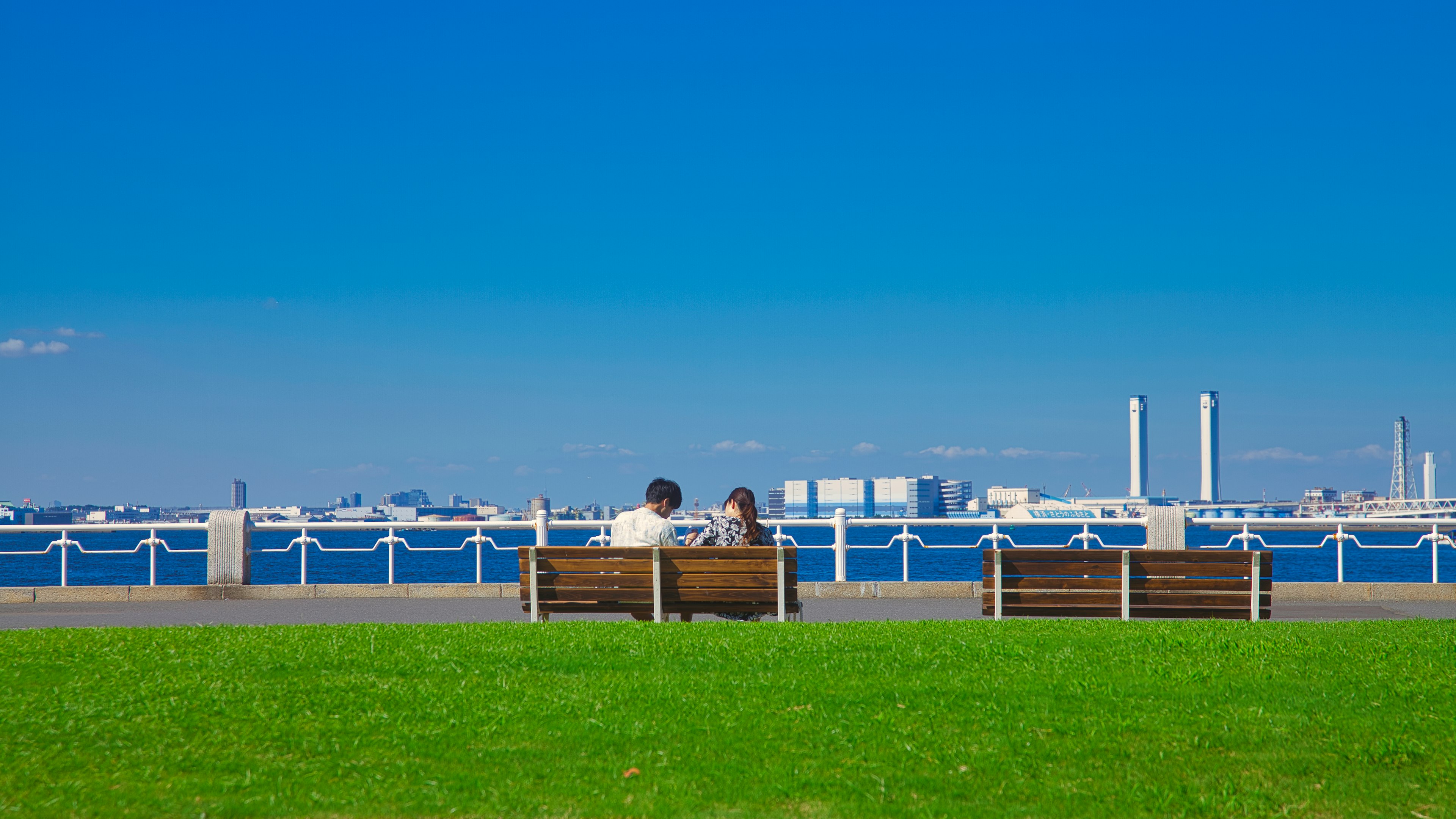 青空の下でベンチに座る二人の人々と海の風景