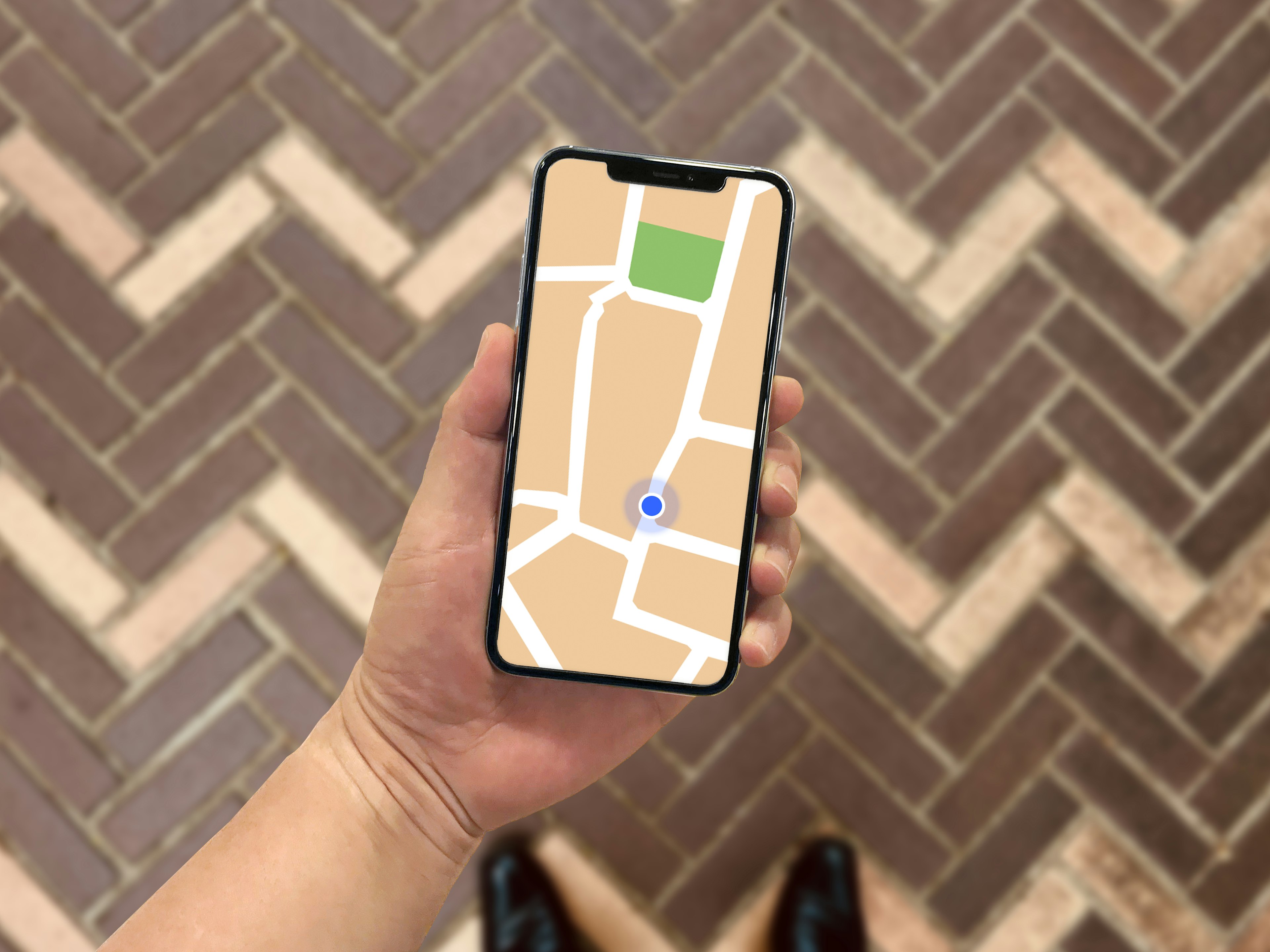 Sebuah smartphone yang menampilkan aplikasi peta dipegang di tangan di atas lantai pola herringbone