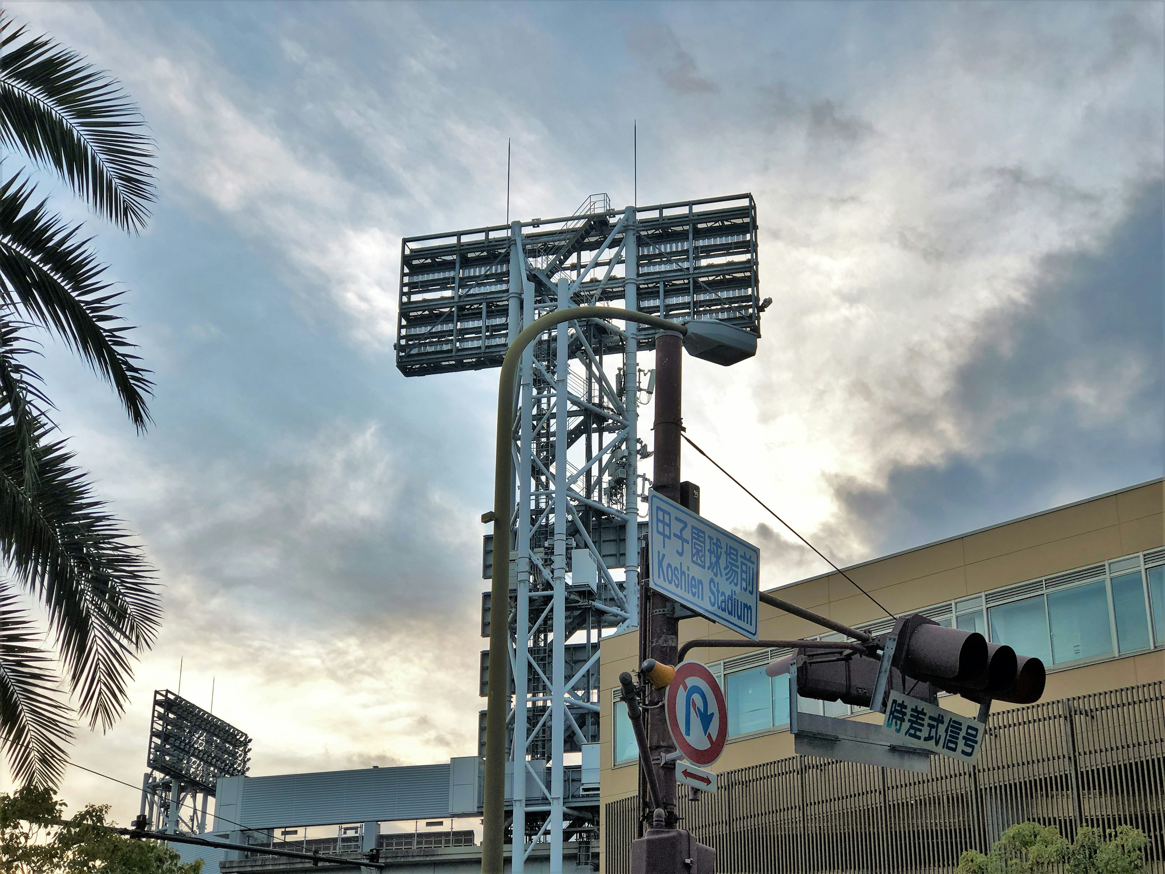 Tall lighting tower with a cloudy sky in the background and a building