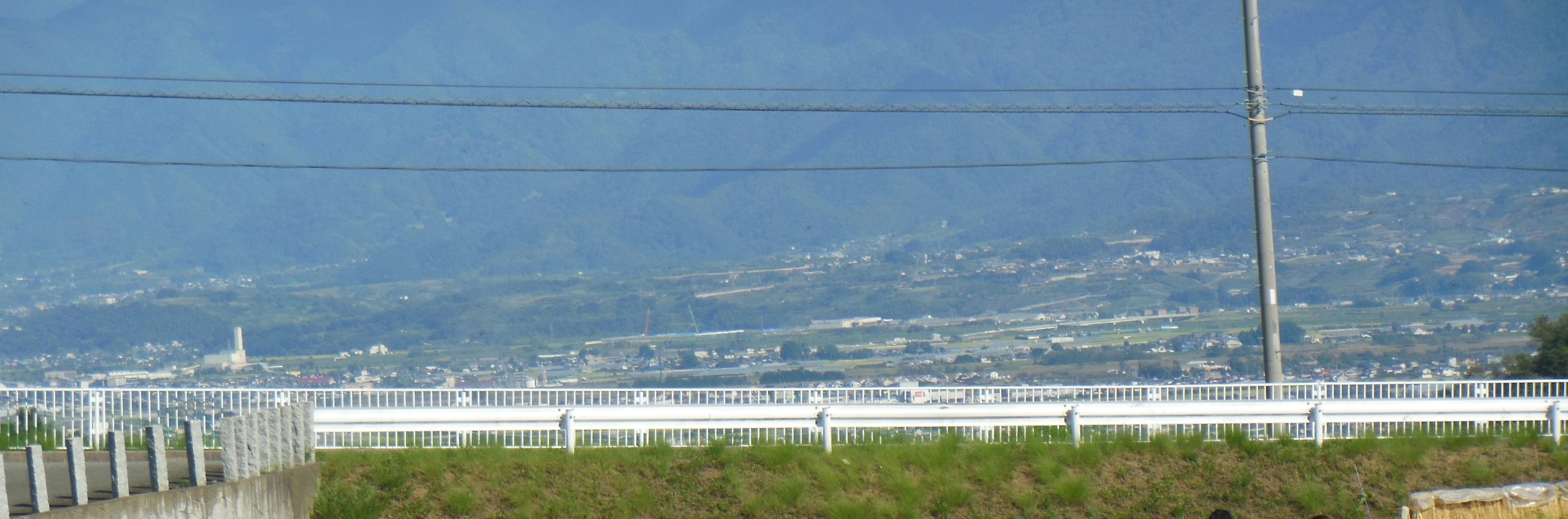 Lanskap perkotaan yang luas dengan langit biru dan gunung di latar belakang serta pagar putih