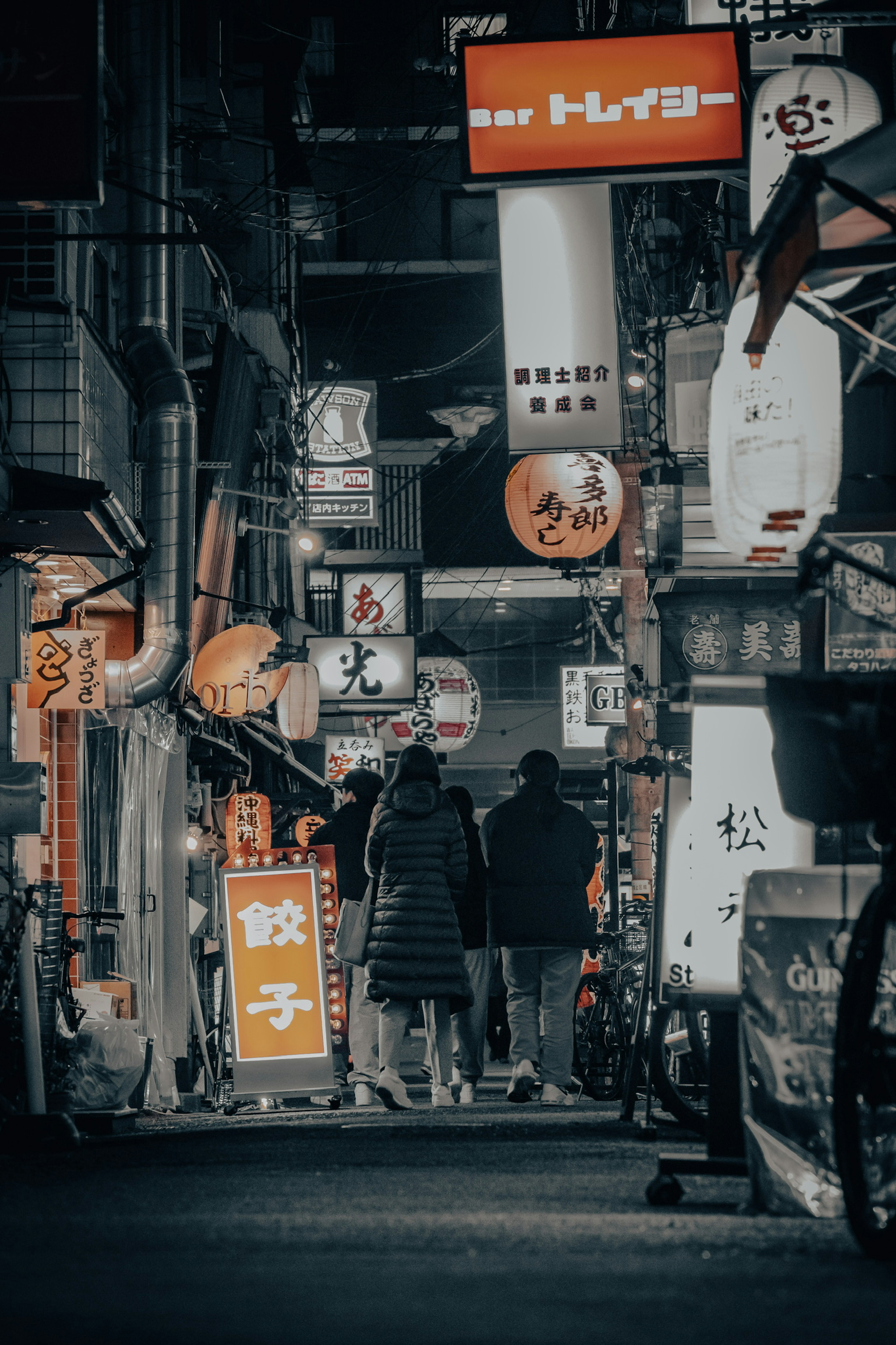 Callejón oscuro con letreros de restaurantes japoneses y siluetas de personas