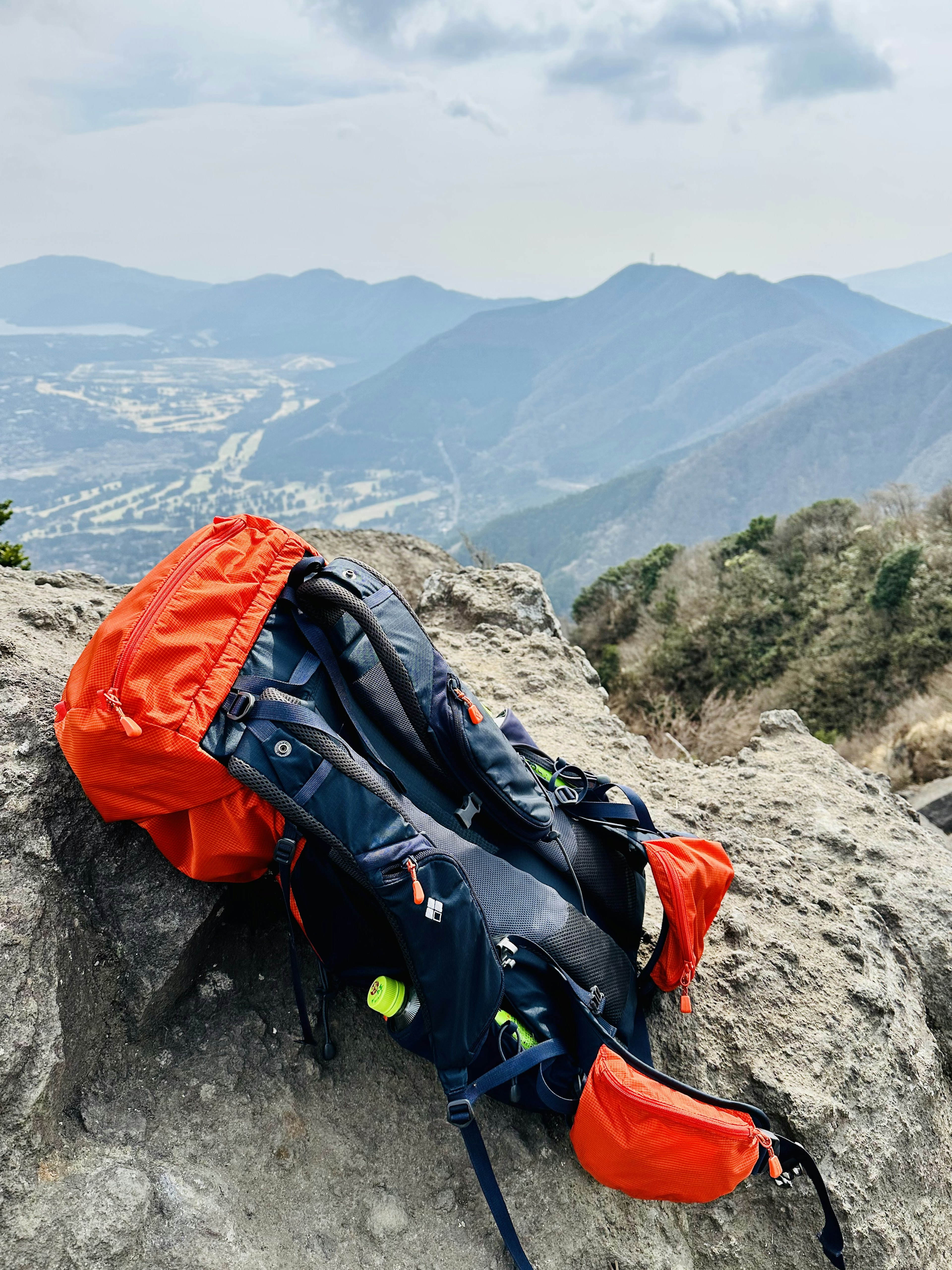 Ein orangefarbener Rucksack liegt auf einem Felsen mit Bergen im Hintergrund