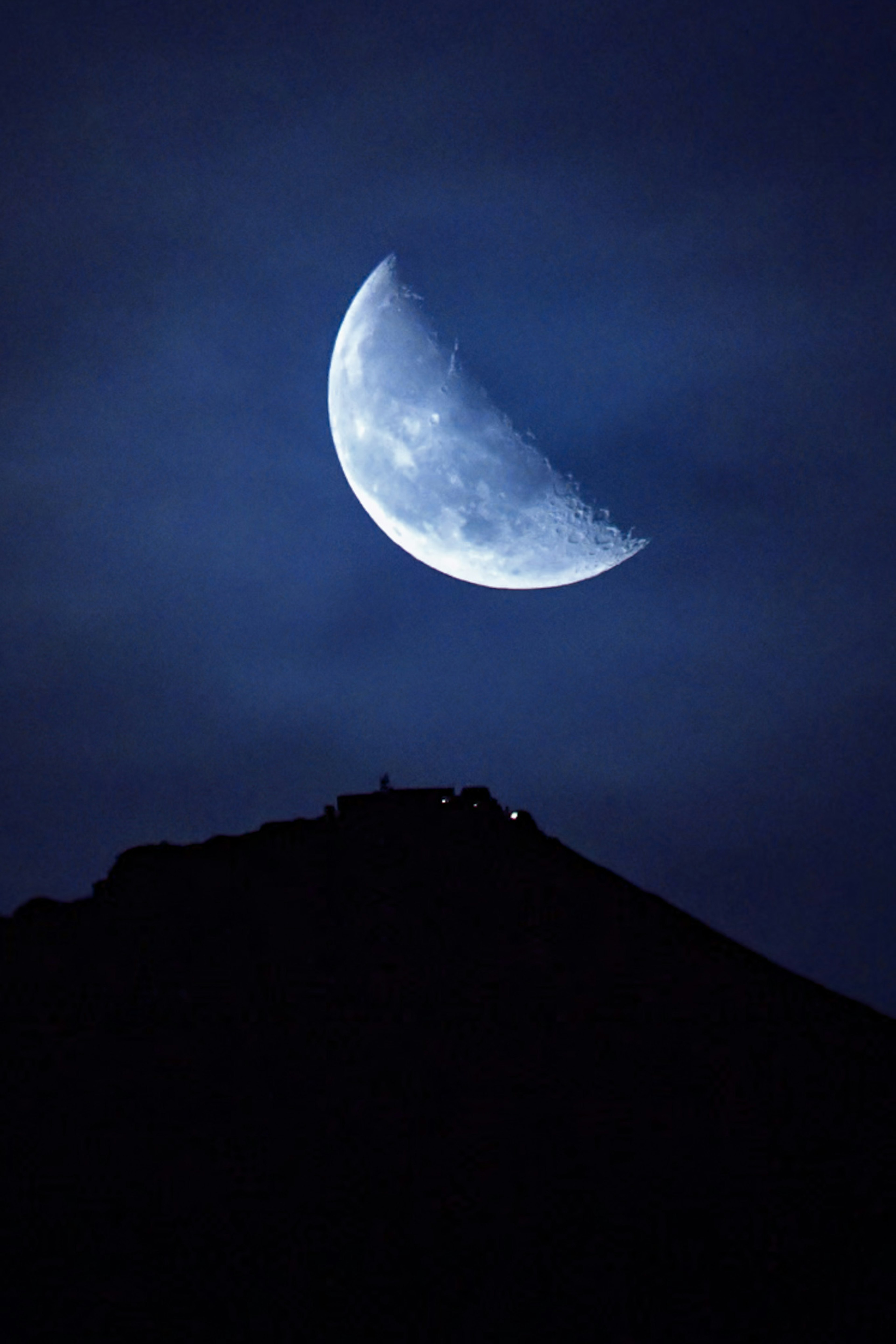 Luna creciente en un cielo nocturno azul sobre la silueta de una montaña