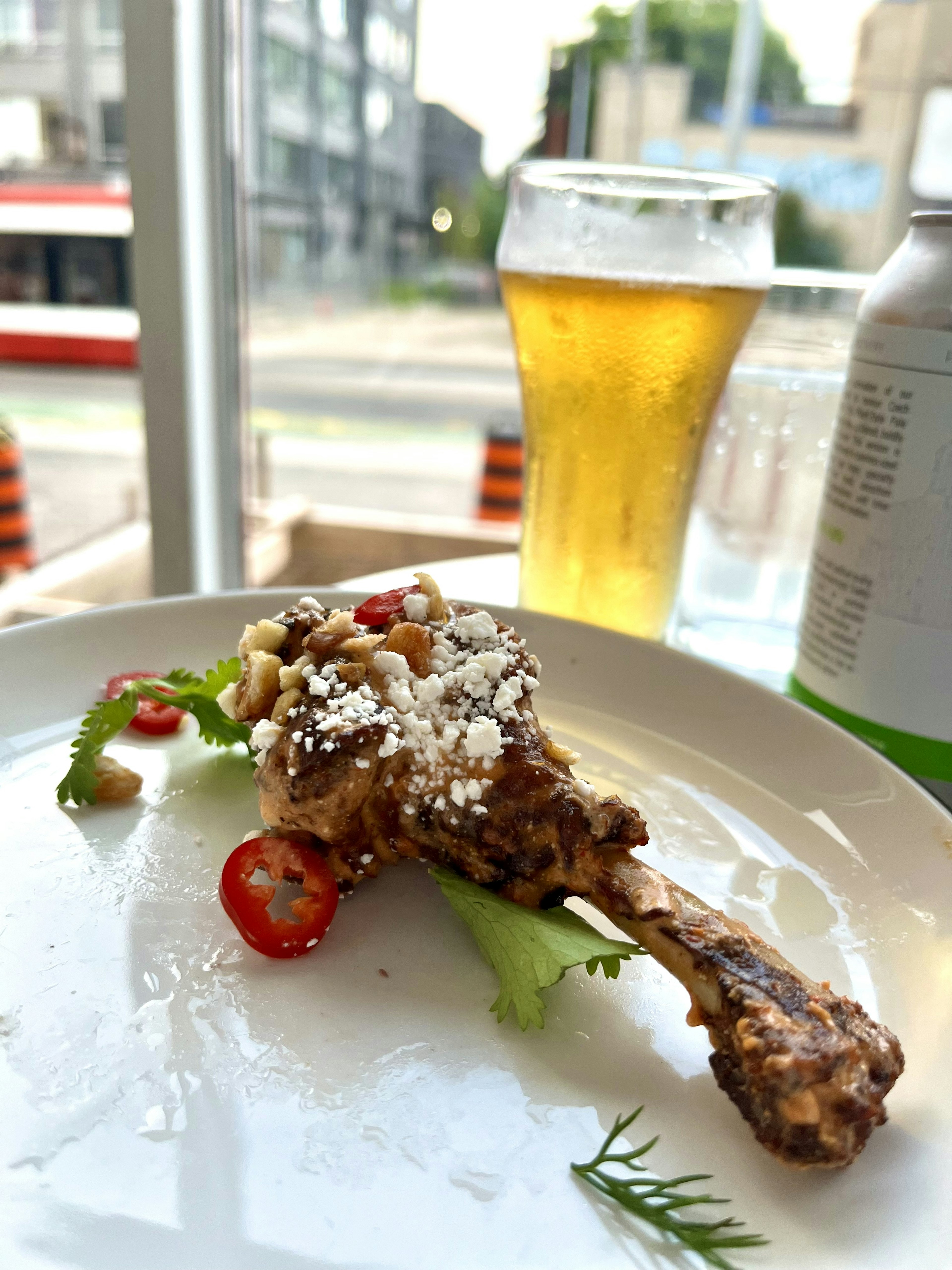 Un plato con un muslo de pollo adornado con hierbas y chile junto a un vaso de cerveza