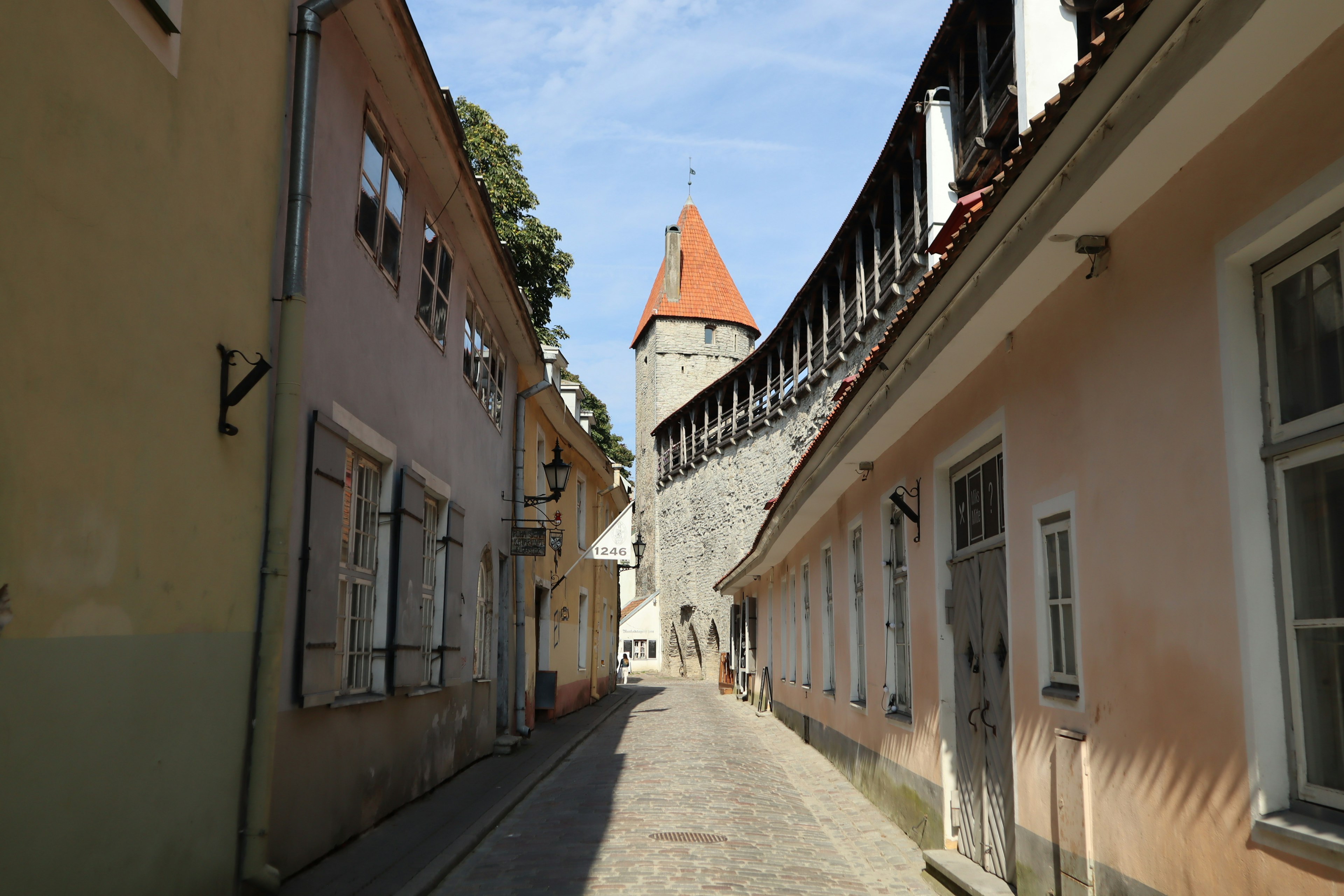 Narrow street lined with old buildings featuring a tower with a pointed roof in the background