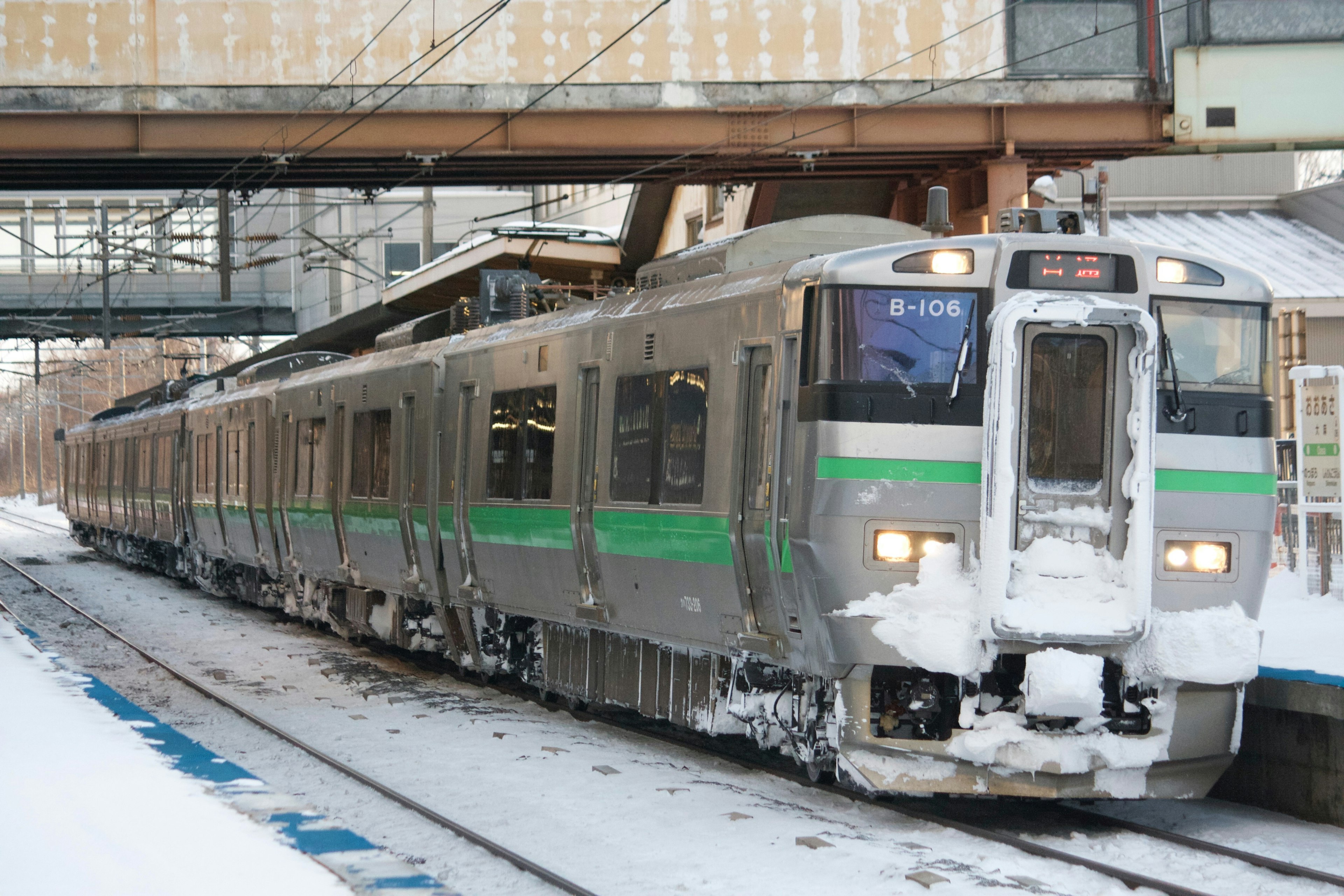 雪に覆われた駅で停車中の緑のラインの銀色の列車