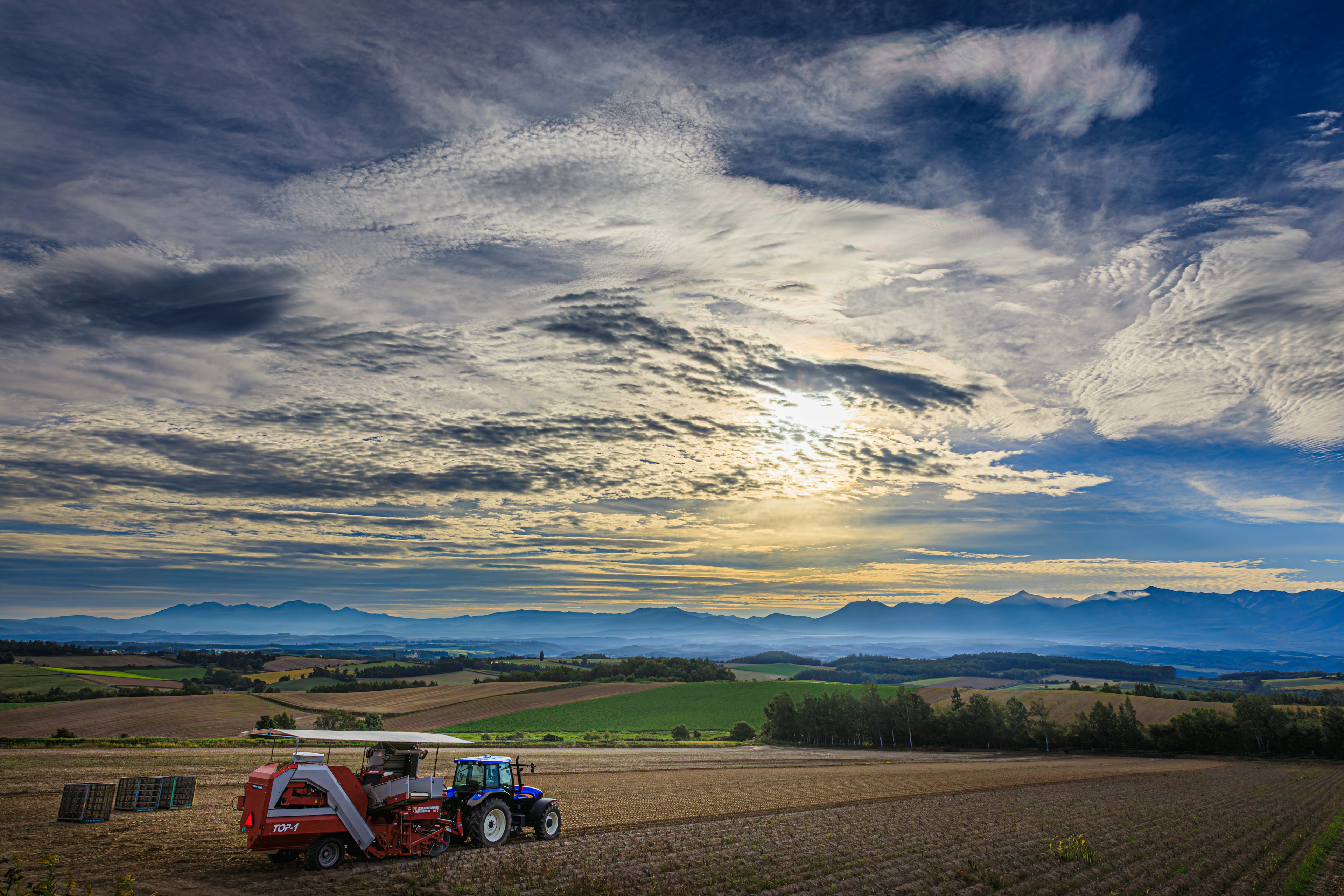 Vista panoramica di un trattore e una mietitrebbia che lavorano in un campo con un cielo al tramonto e montagne sullo sfondo