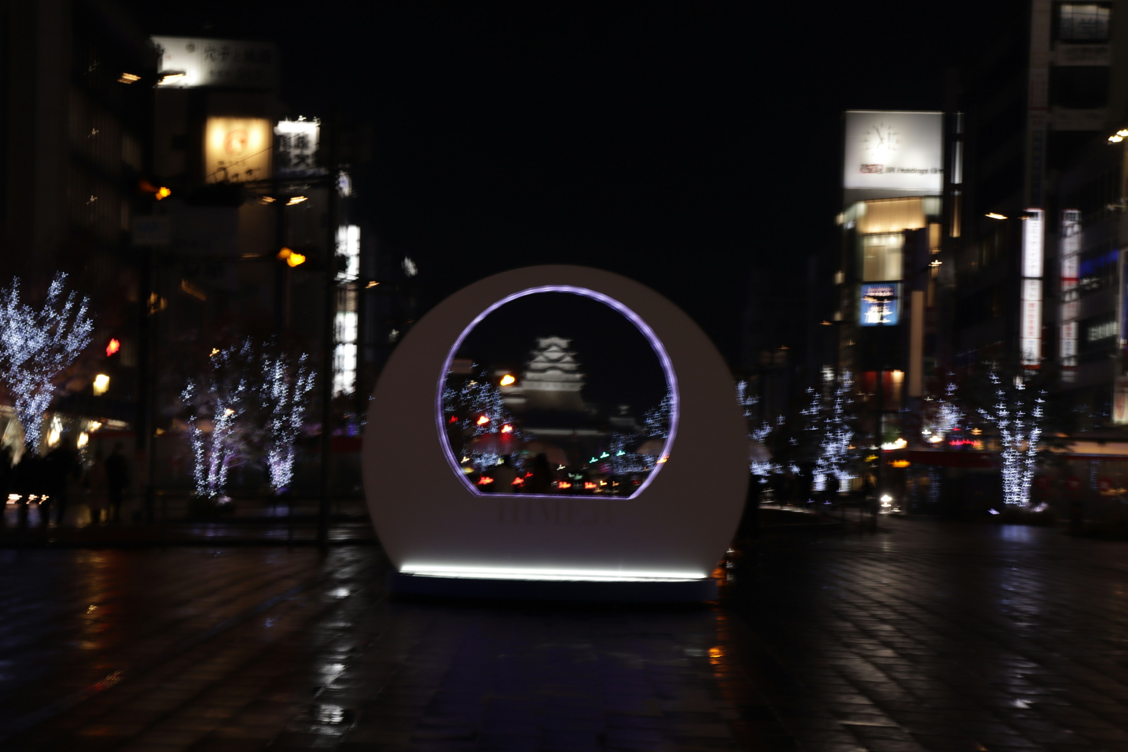 Circular monument with illuminated trees and city lights at night