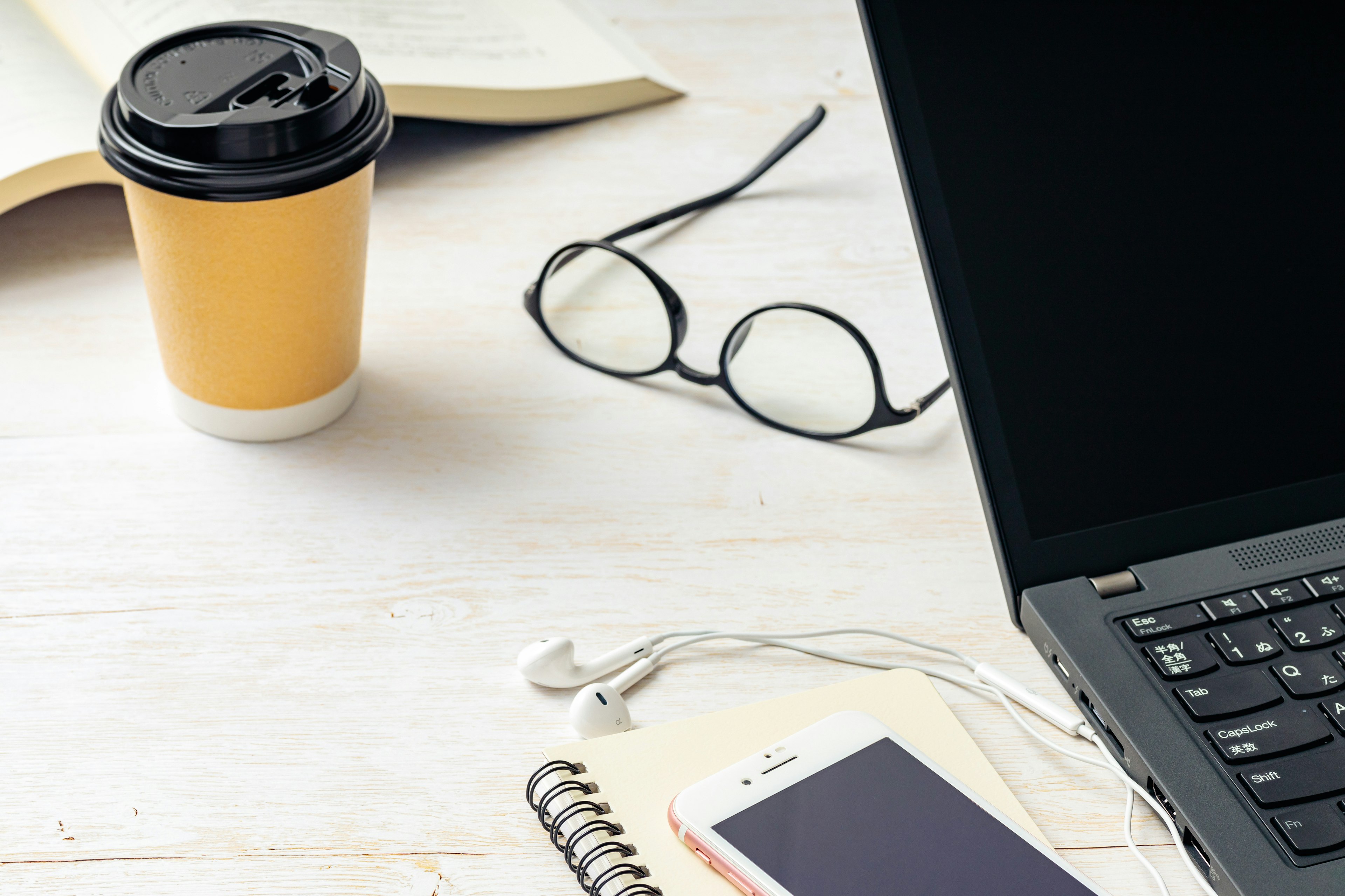 Laptop on a desk with a coffee cup glasses and a smartphone visible