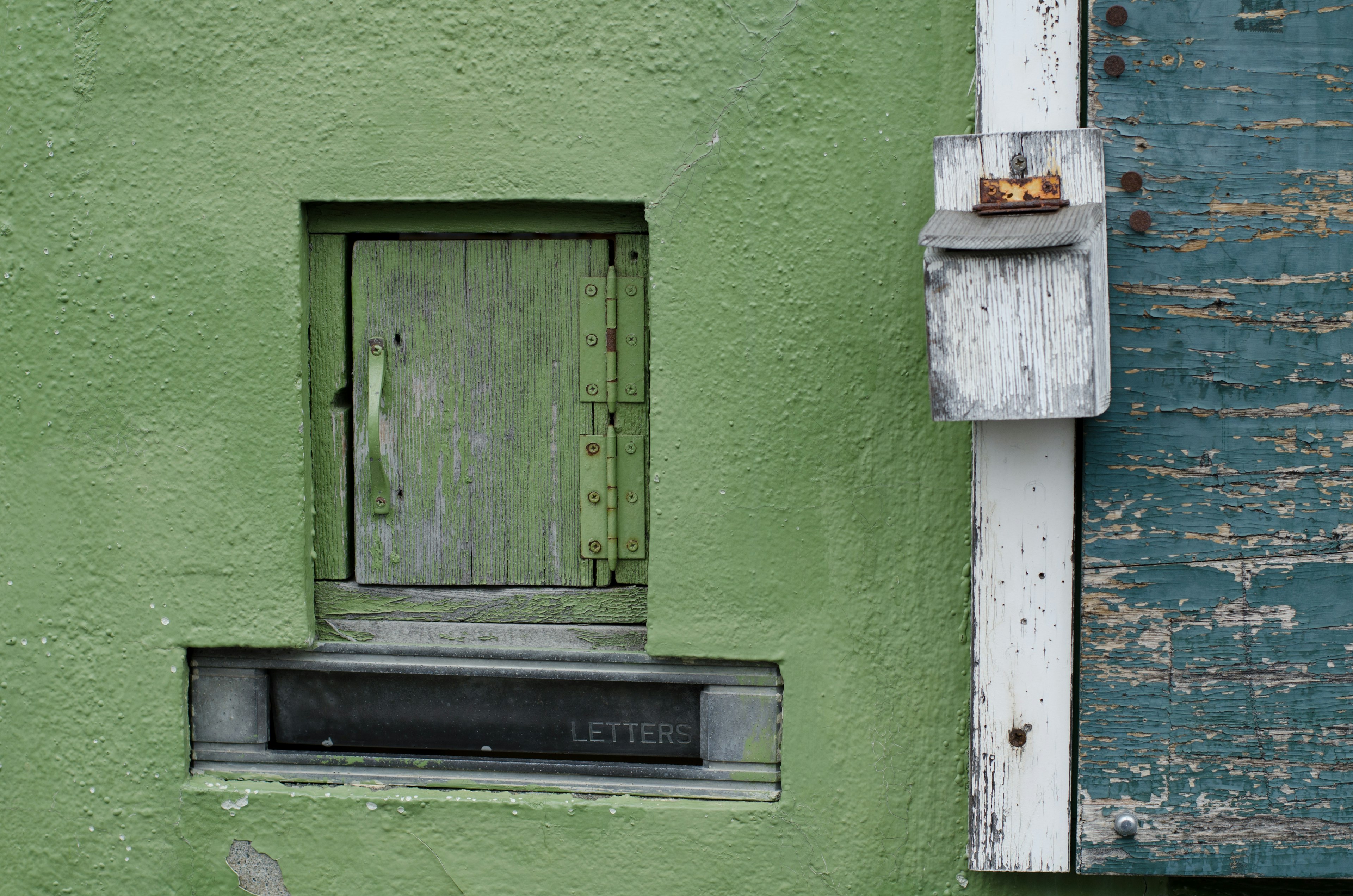 Pequeña ventana de madera y buzón en una pared verde