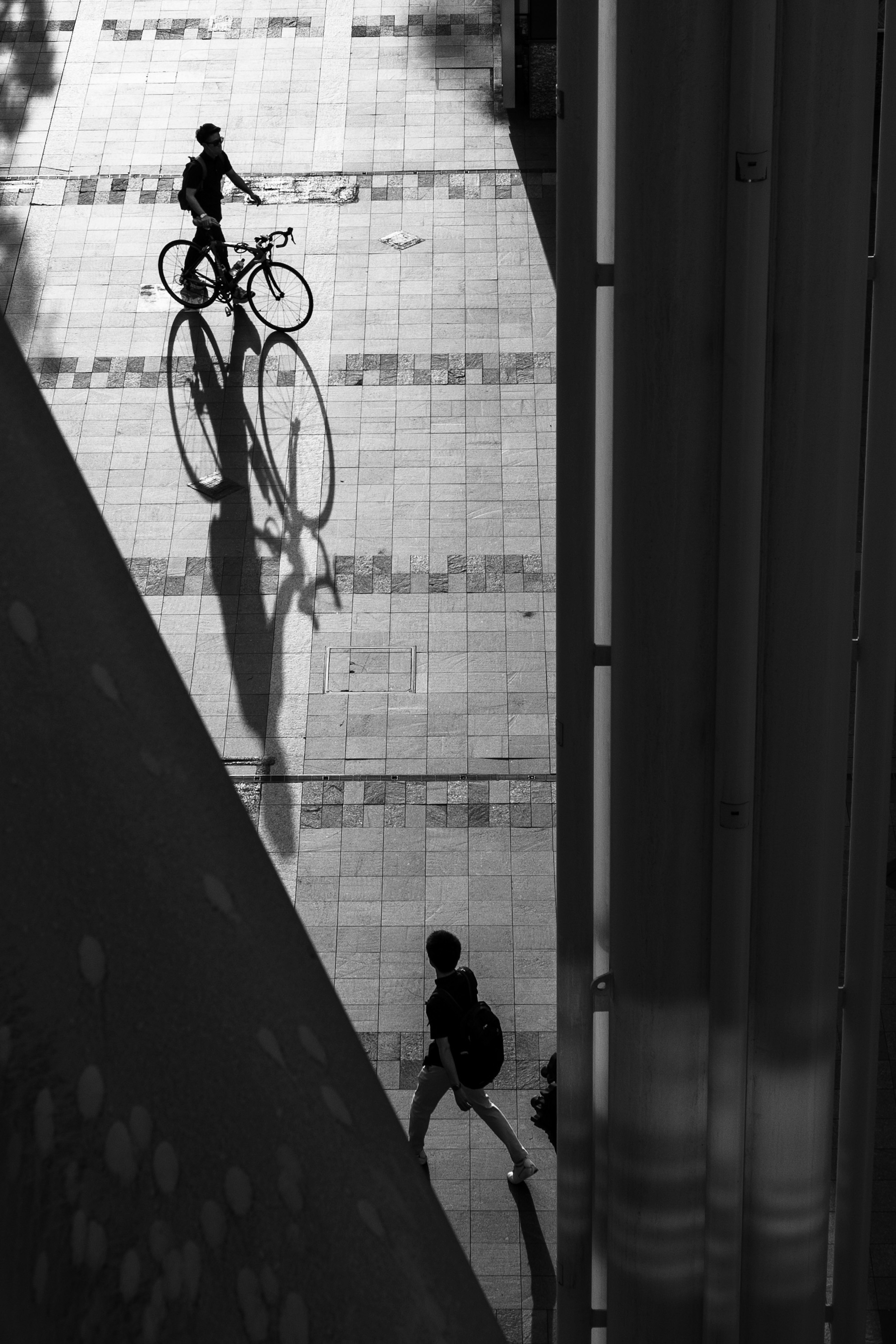 自転車に乗る人物と歩行者の影が映るモノクロの都市風景