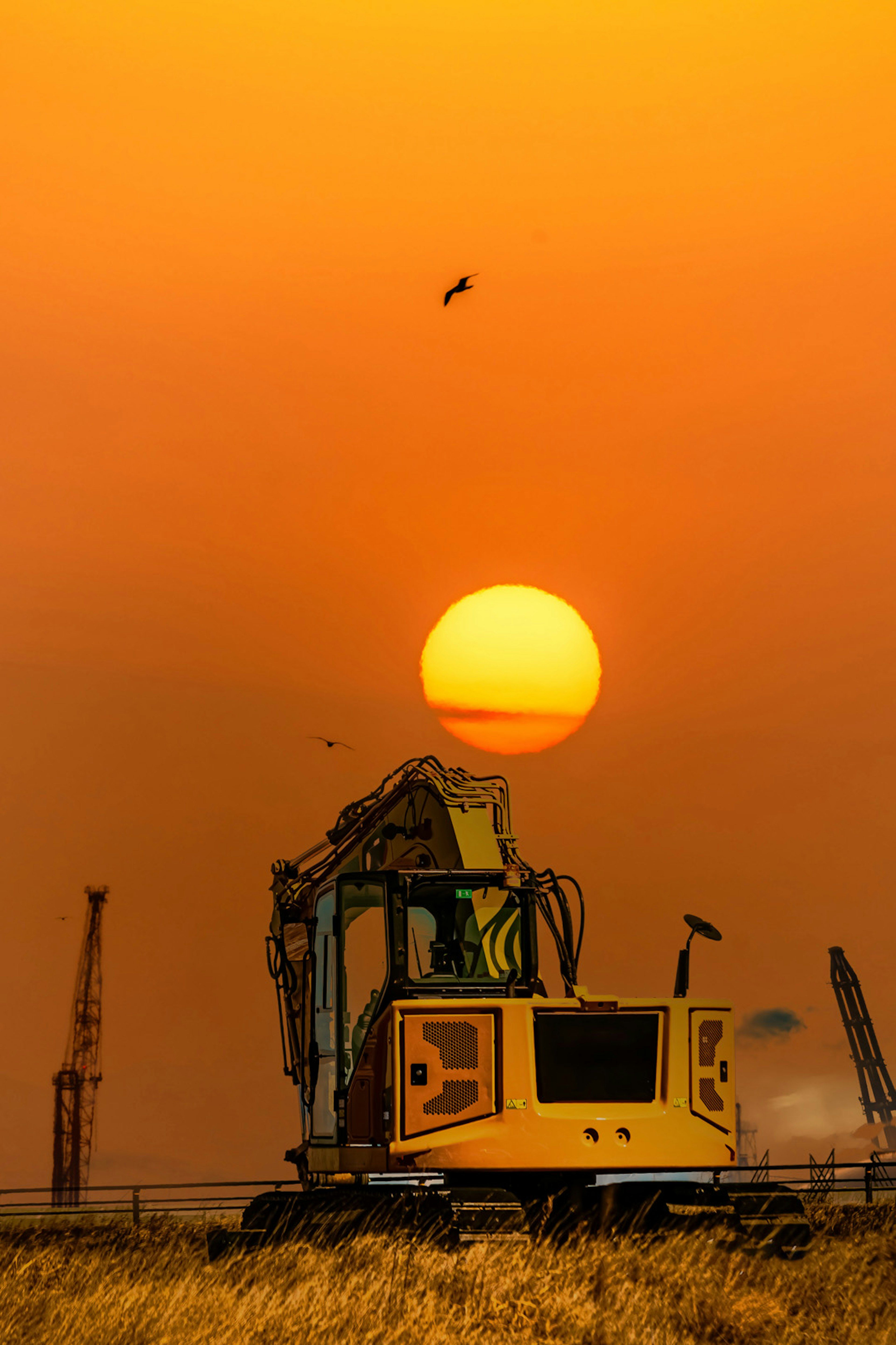 夕日を背景にした黄色い掘削機とオレンジ色の空