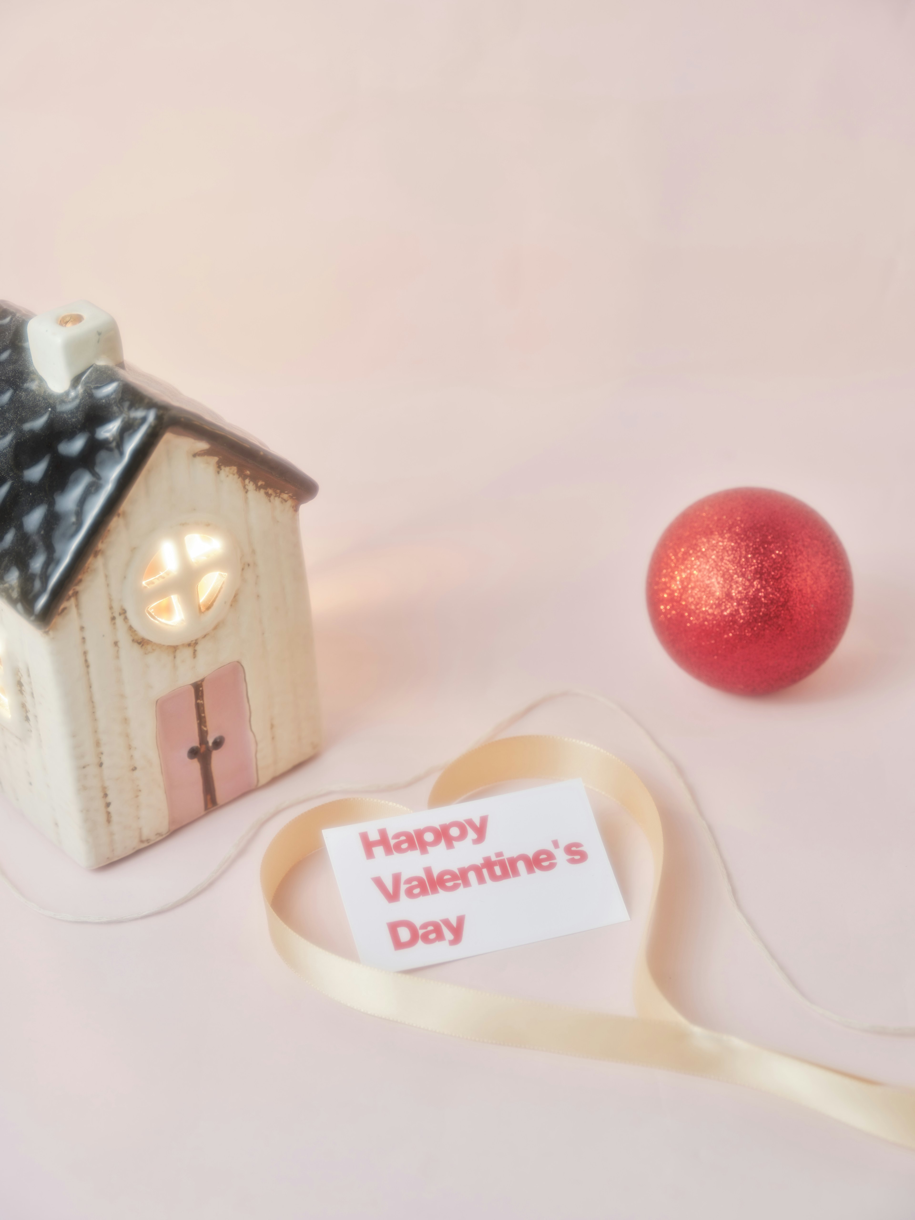 A small decorative house with a window and a red ball nearby with a ribbon saying Happy Valentine's Day