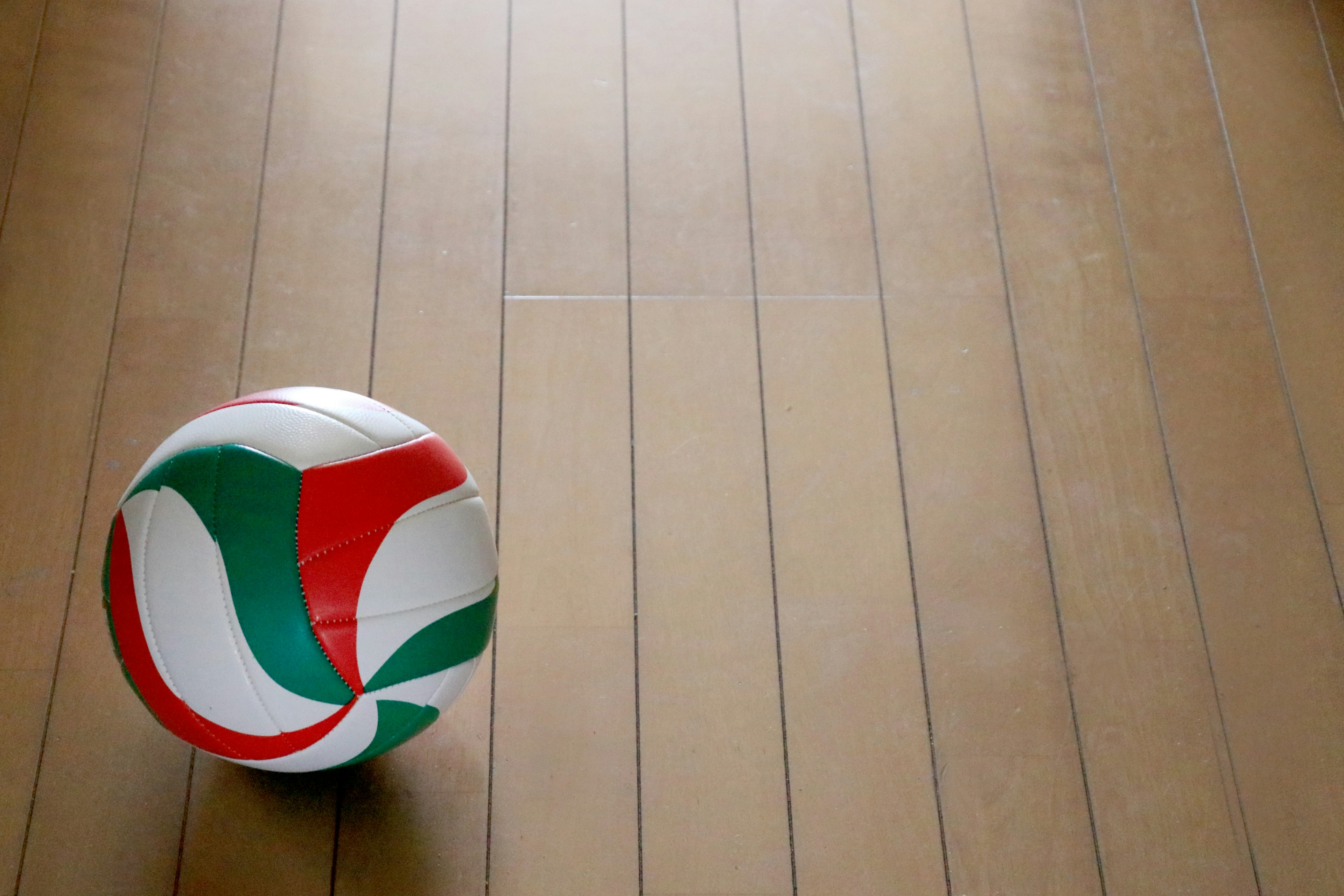 A volleyball with red and green design resting on wooden flooring