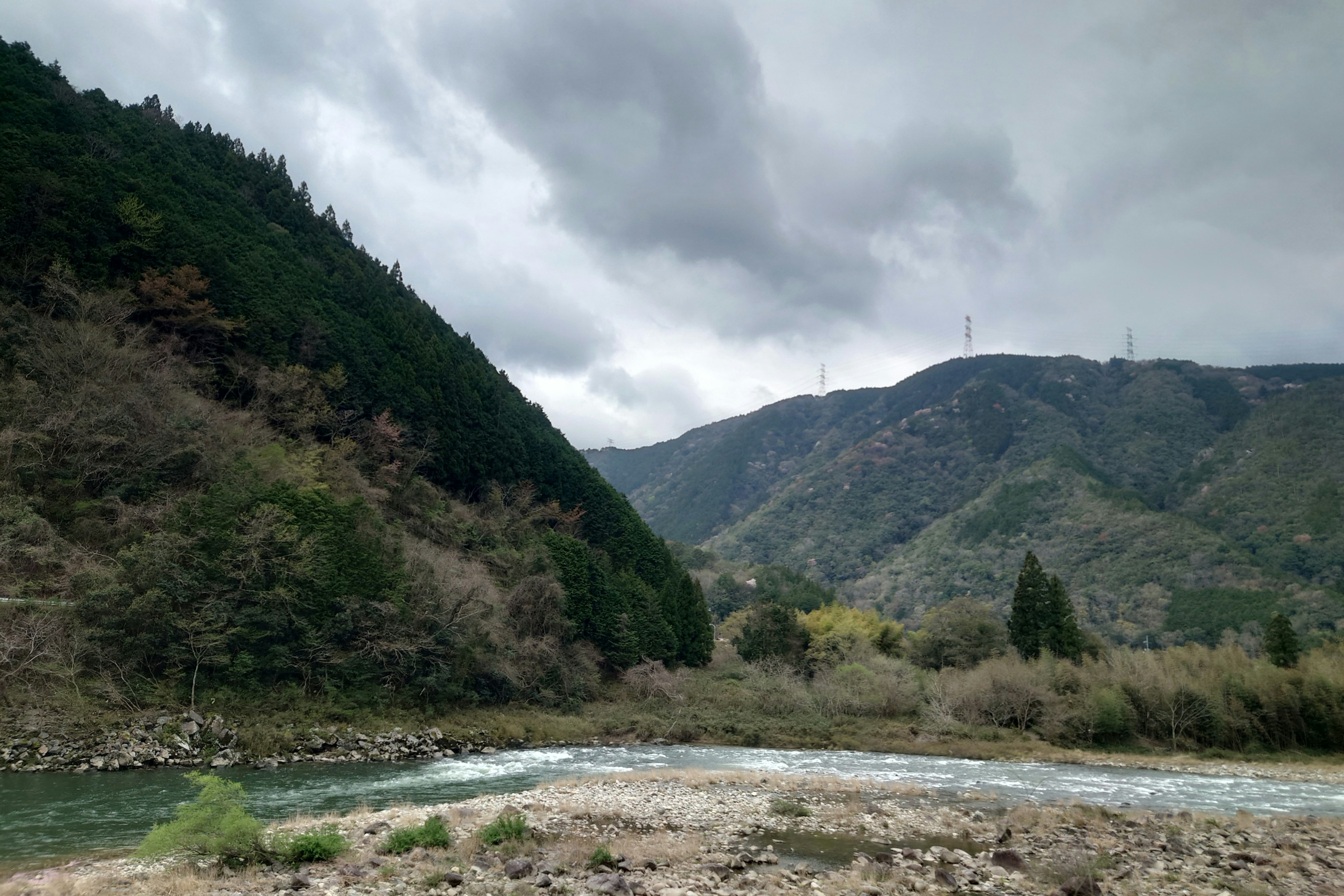 Pemandangan pegunungan dan sungai di bawah langit mendung dengan hutan hijau subur