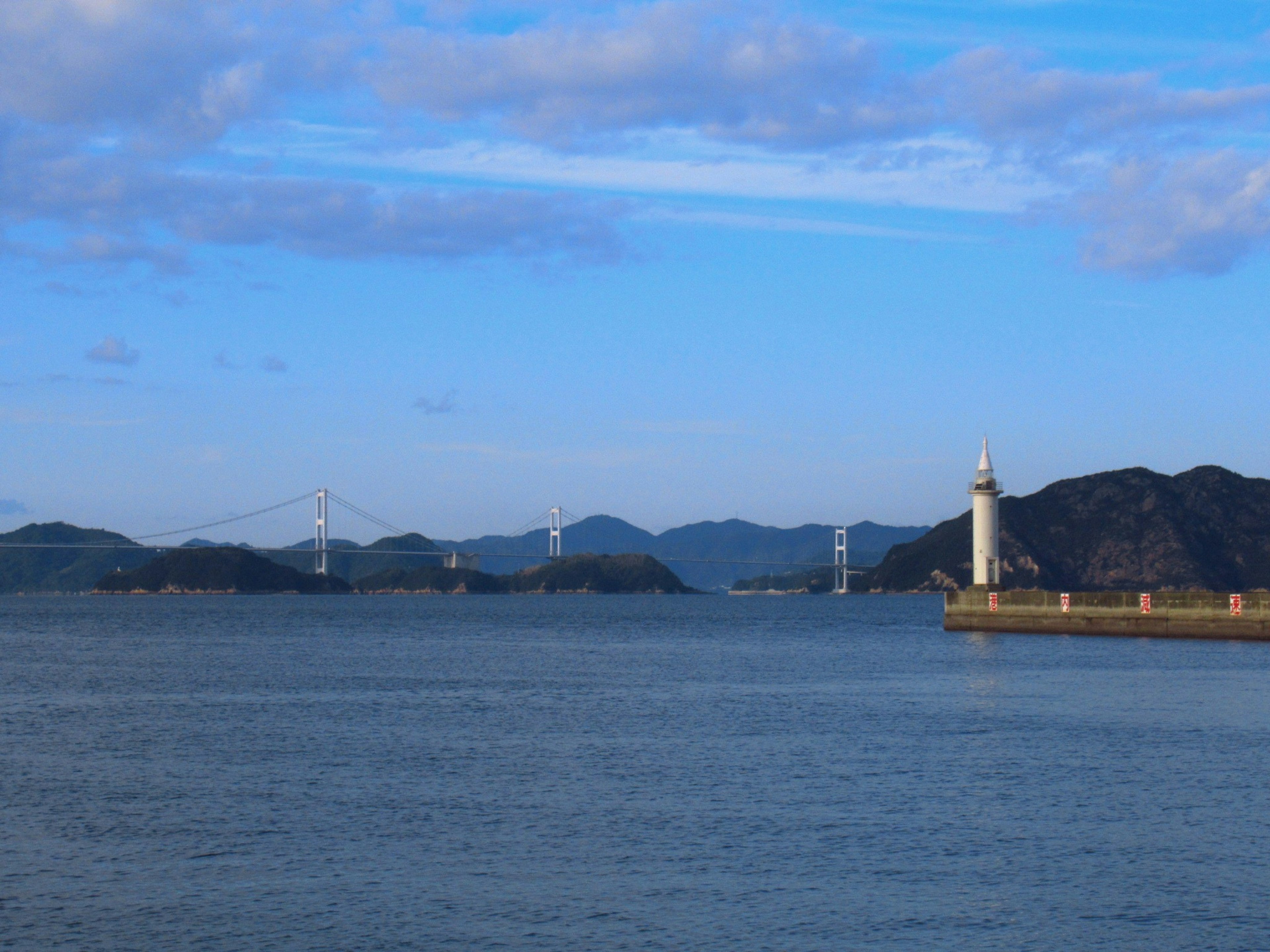 海と灯台の風景に青い空と山々が広がる