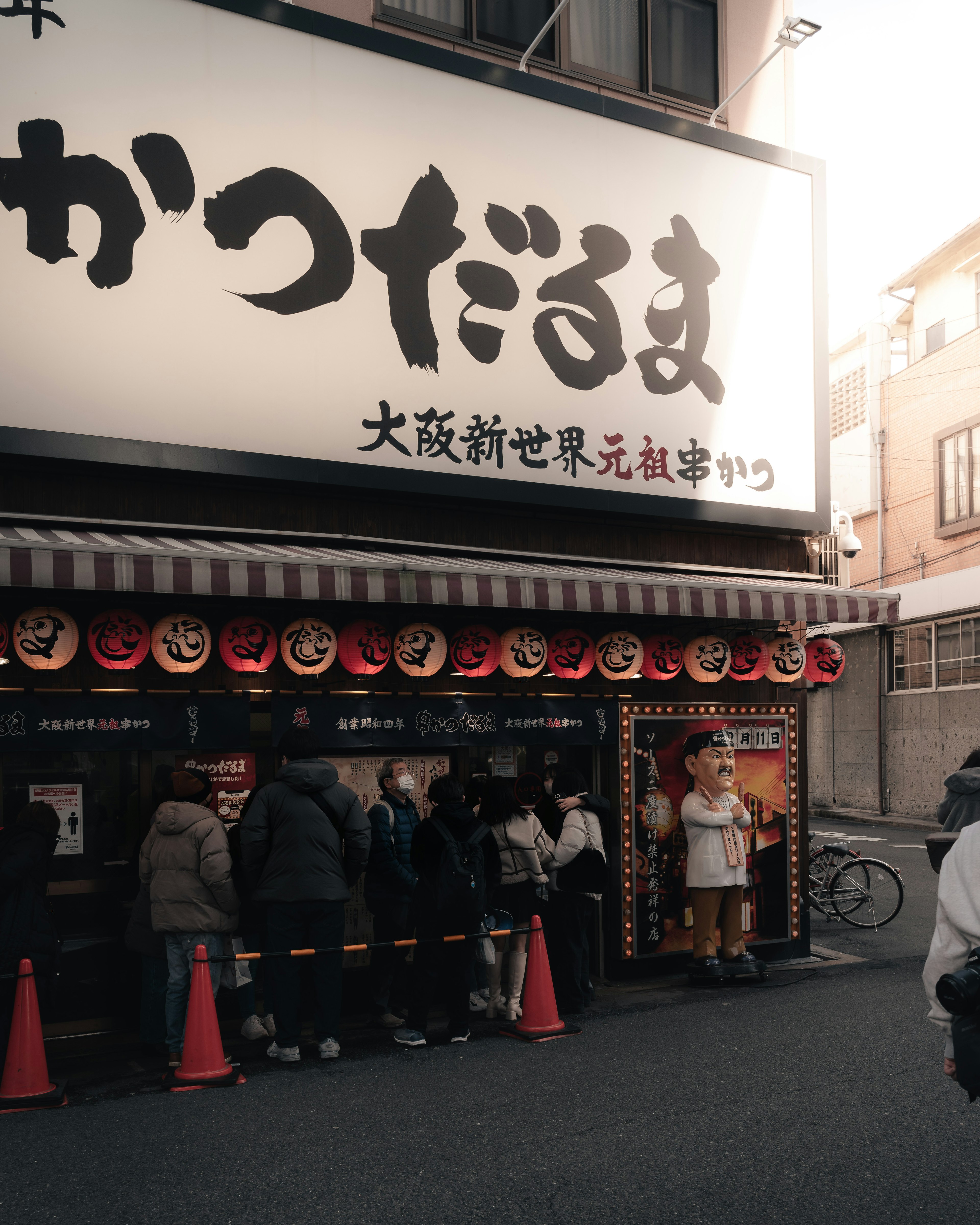 Exterior of a restaurant with a long queue large sign and red lanterns