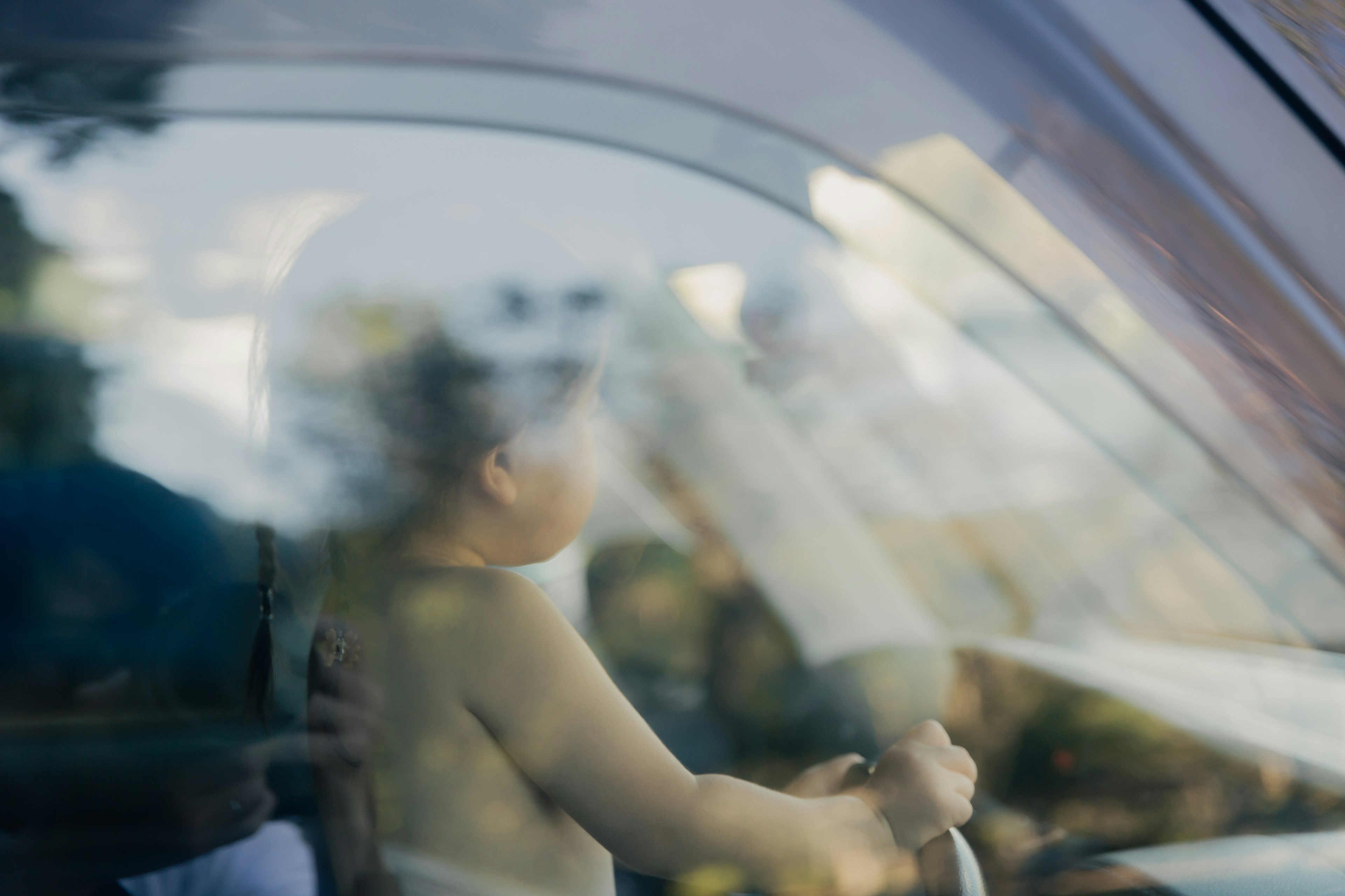 A baby seen from the side inside a car with a blurred background and view through the window