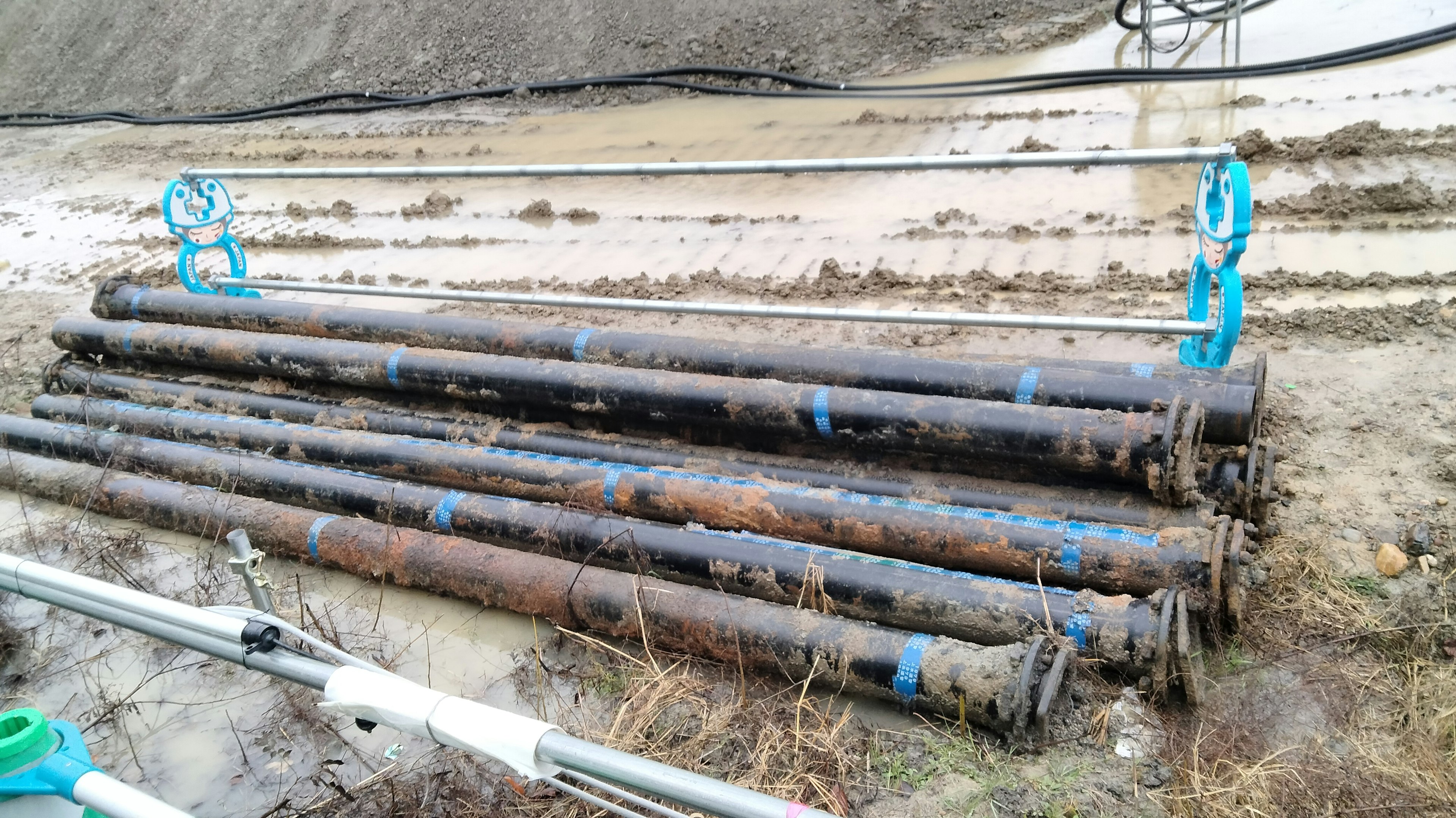 Rusty metal pipes with blue handles resting on wet ground