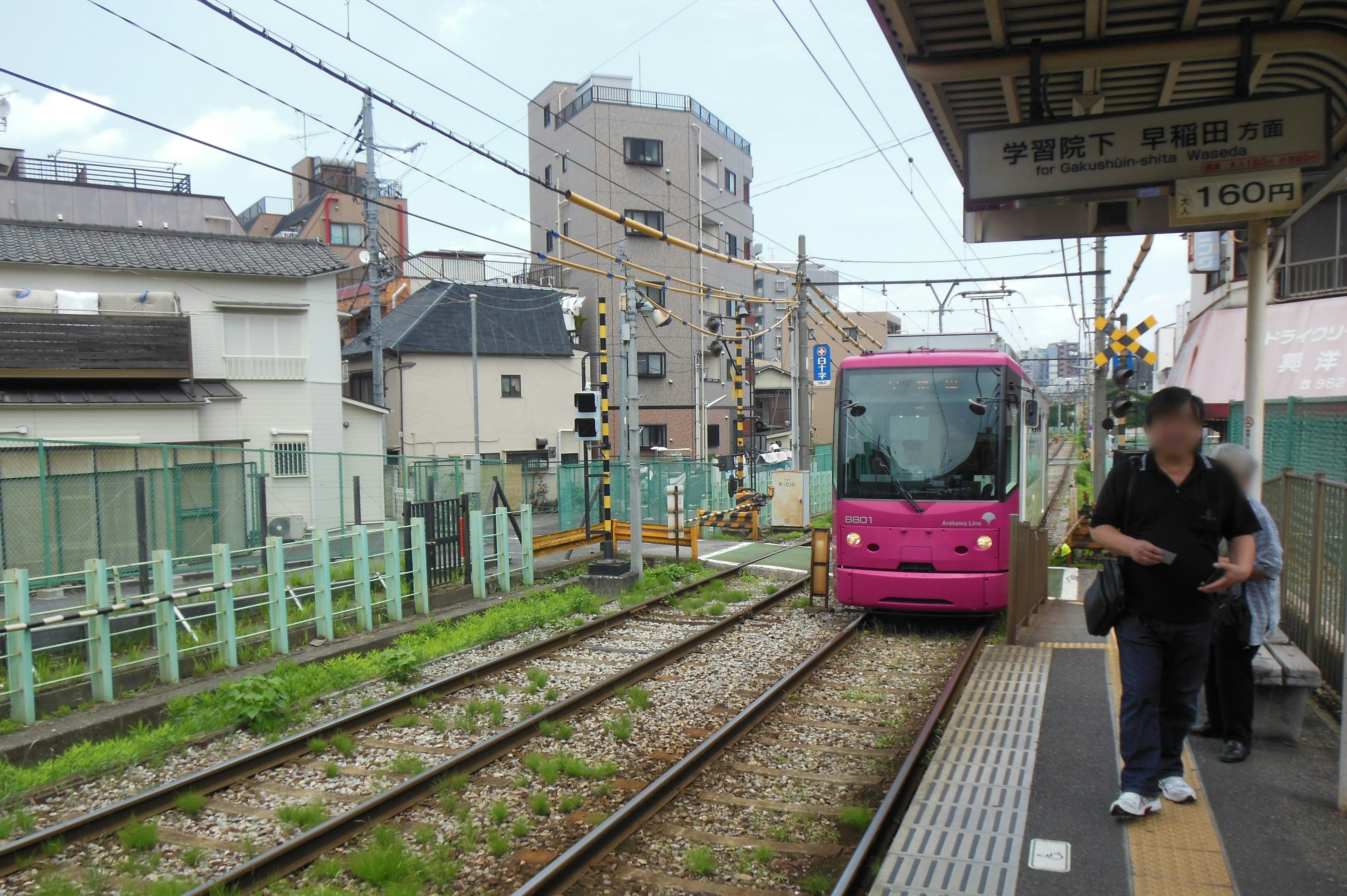 A pink train stopped at a station with visible tracks and buildings