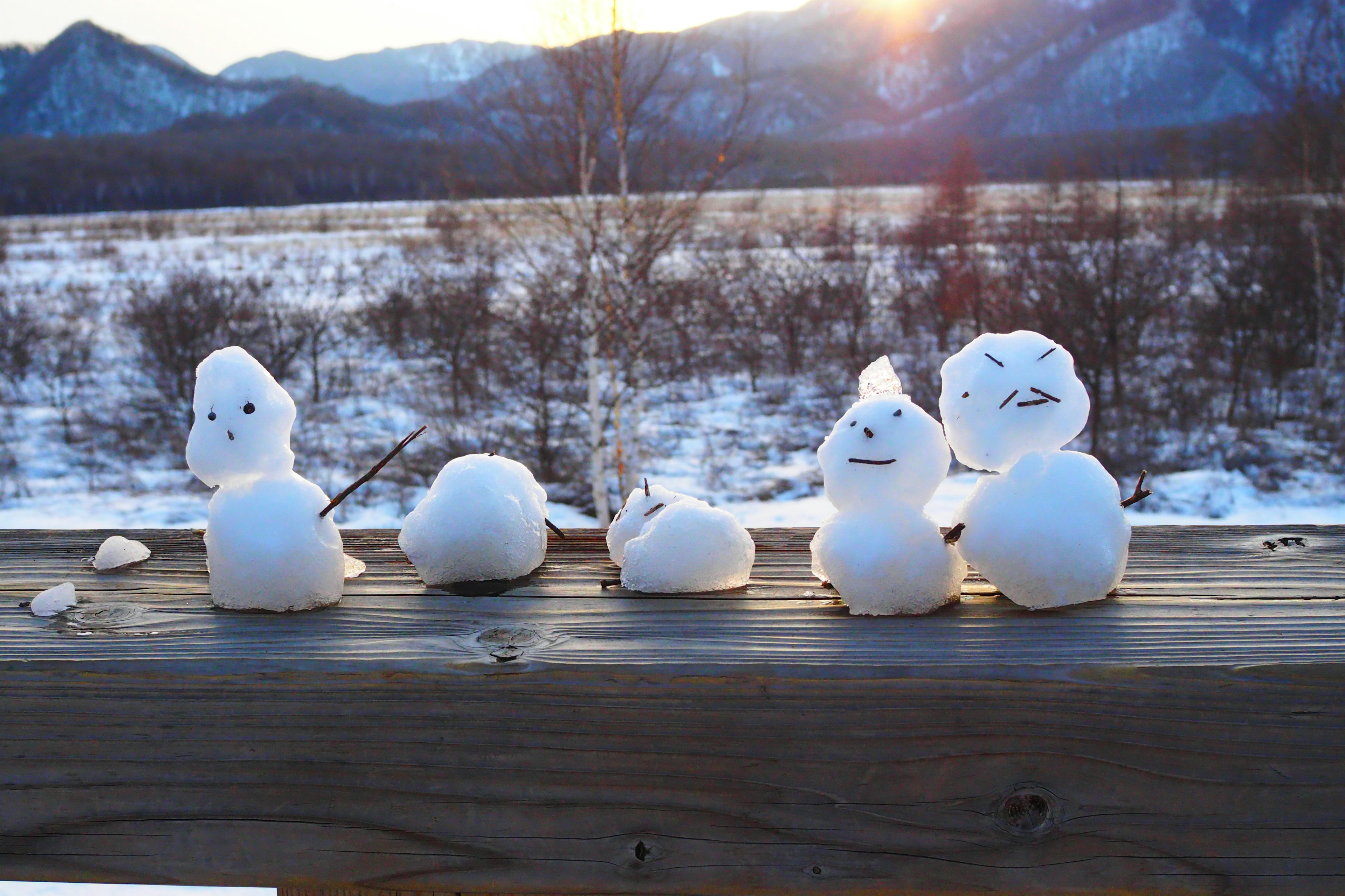 Una fila di pupazzi di neve con un tramonto sullo sfondo di montagne