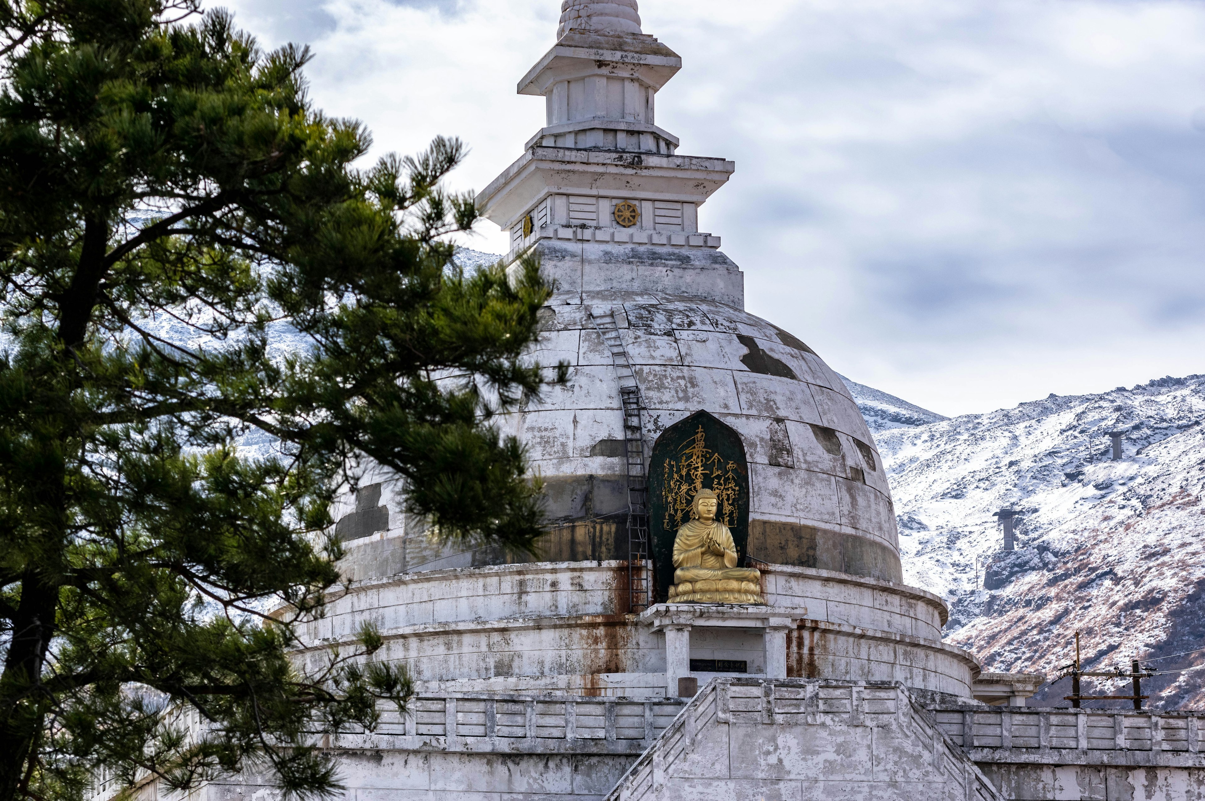 Stupa with a Buddha statue set against snowy mountains