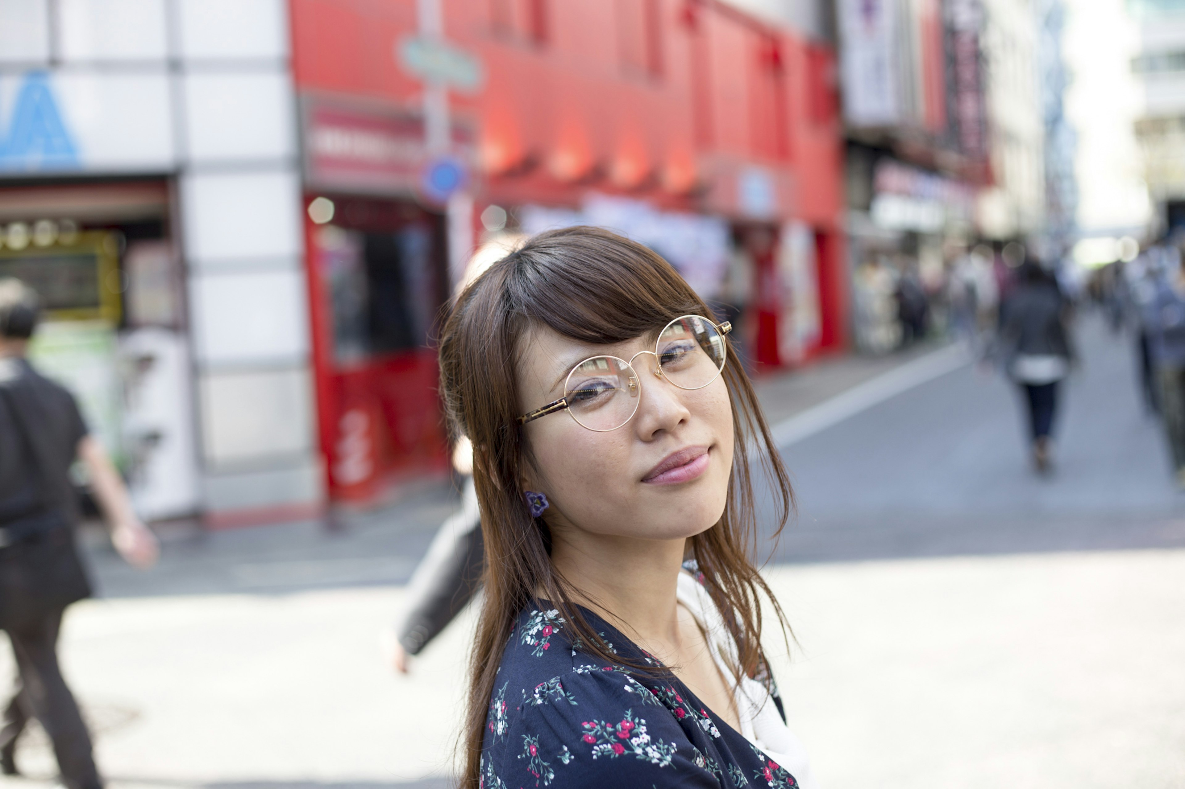 Mujer mirando hacia atrás en la calle usando gafas y un vestido floral con edificios rojos de fondo