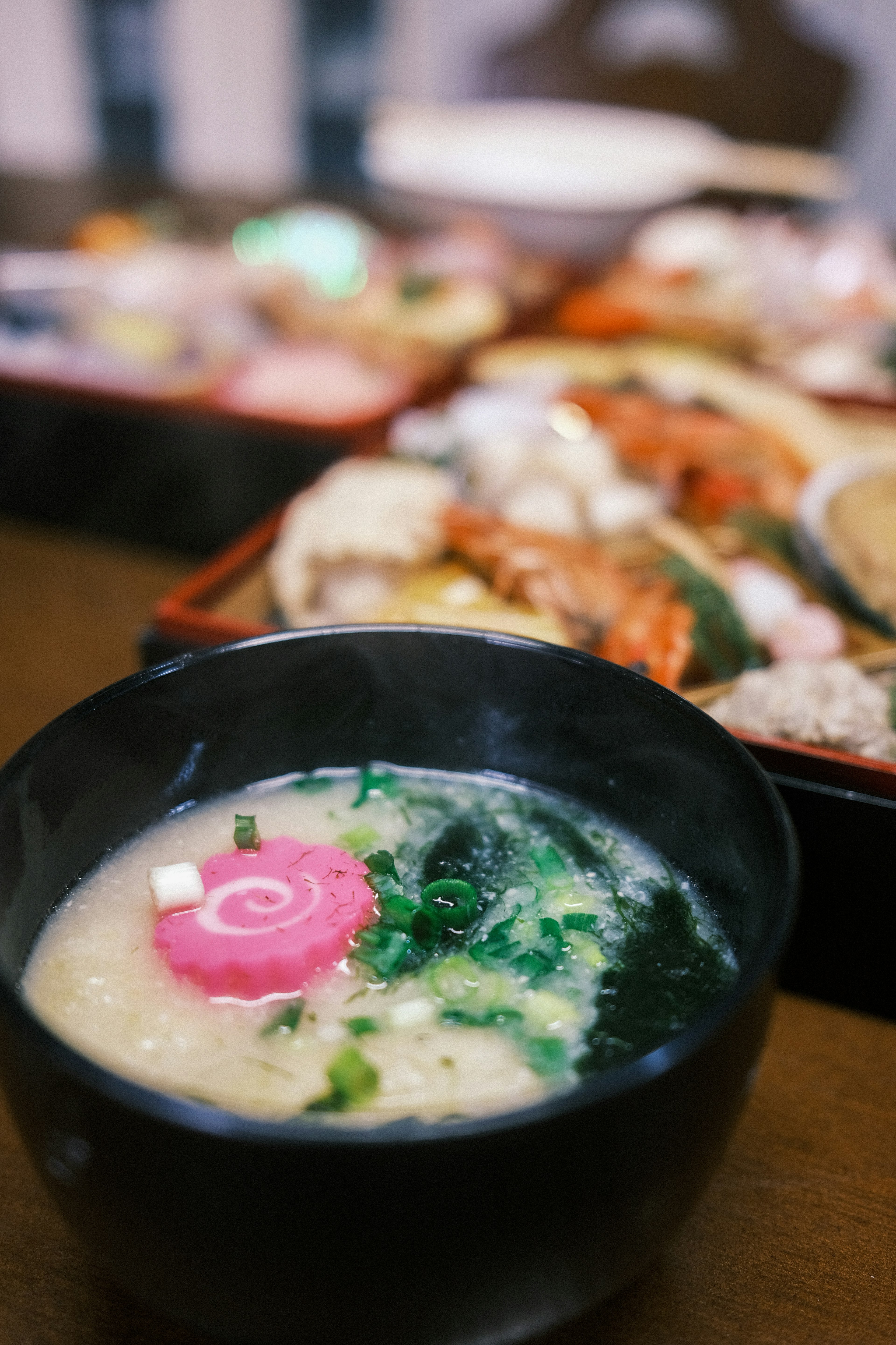 Miso soup in a black bowl topped with green onions and a pink swirl fish cake