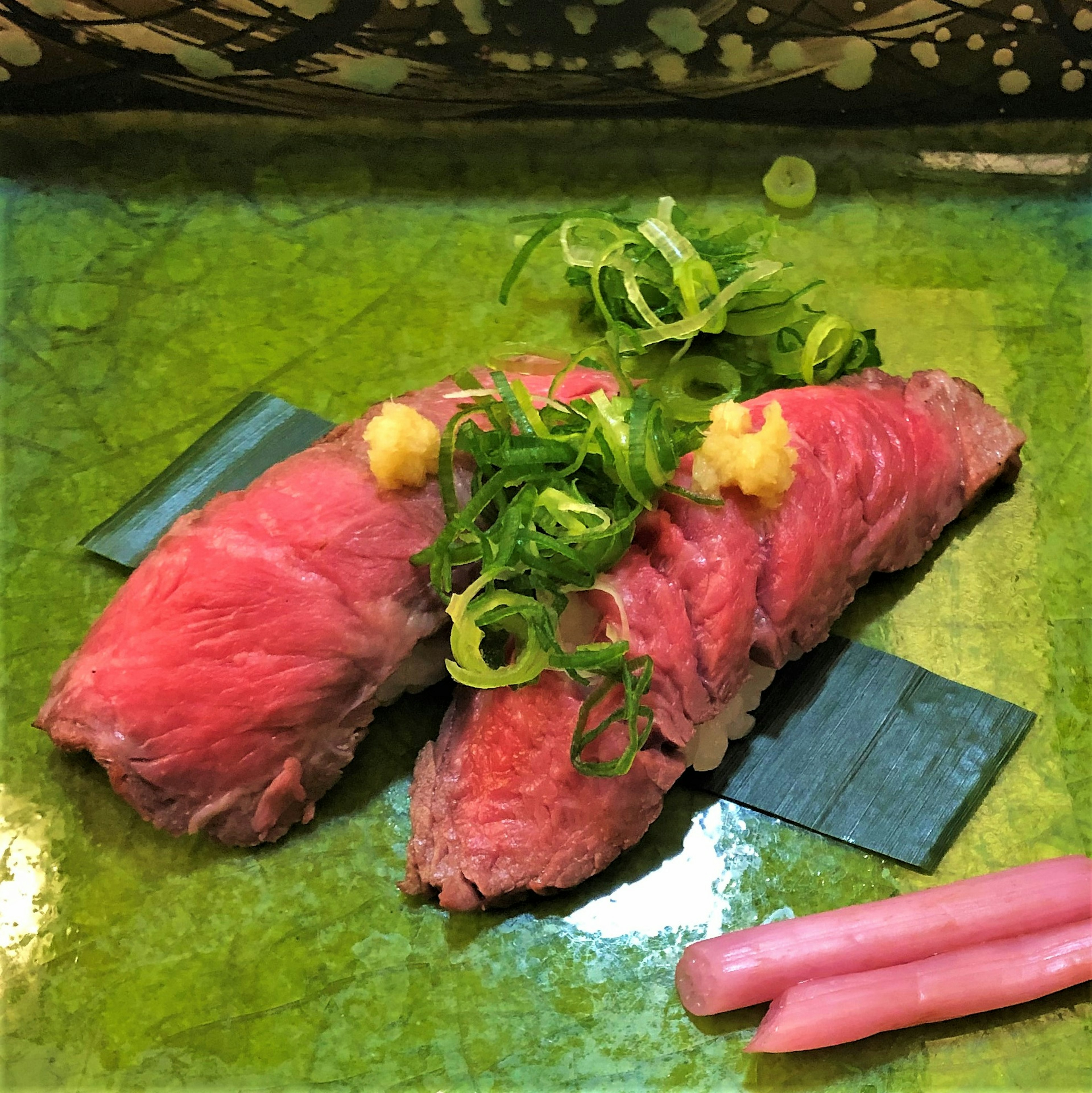 Sushi with vibrant red fish topped with green onions and ginger on a green plate