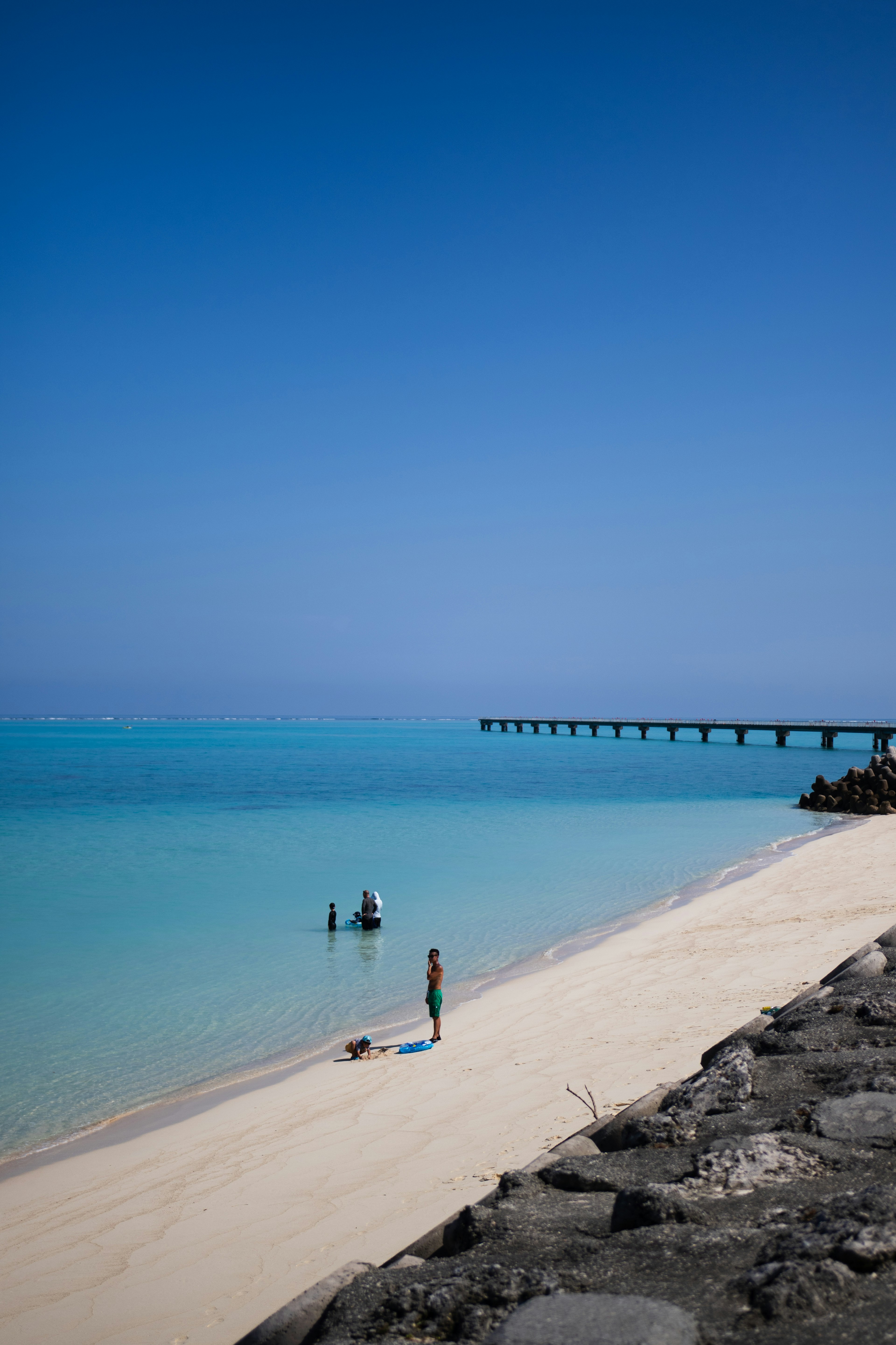 Pantai indah dengan air biru jernih dan dermaga di kejauhan