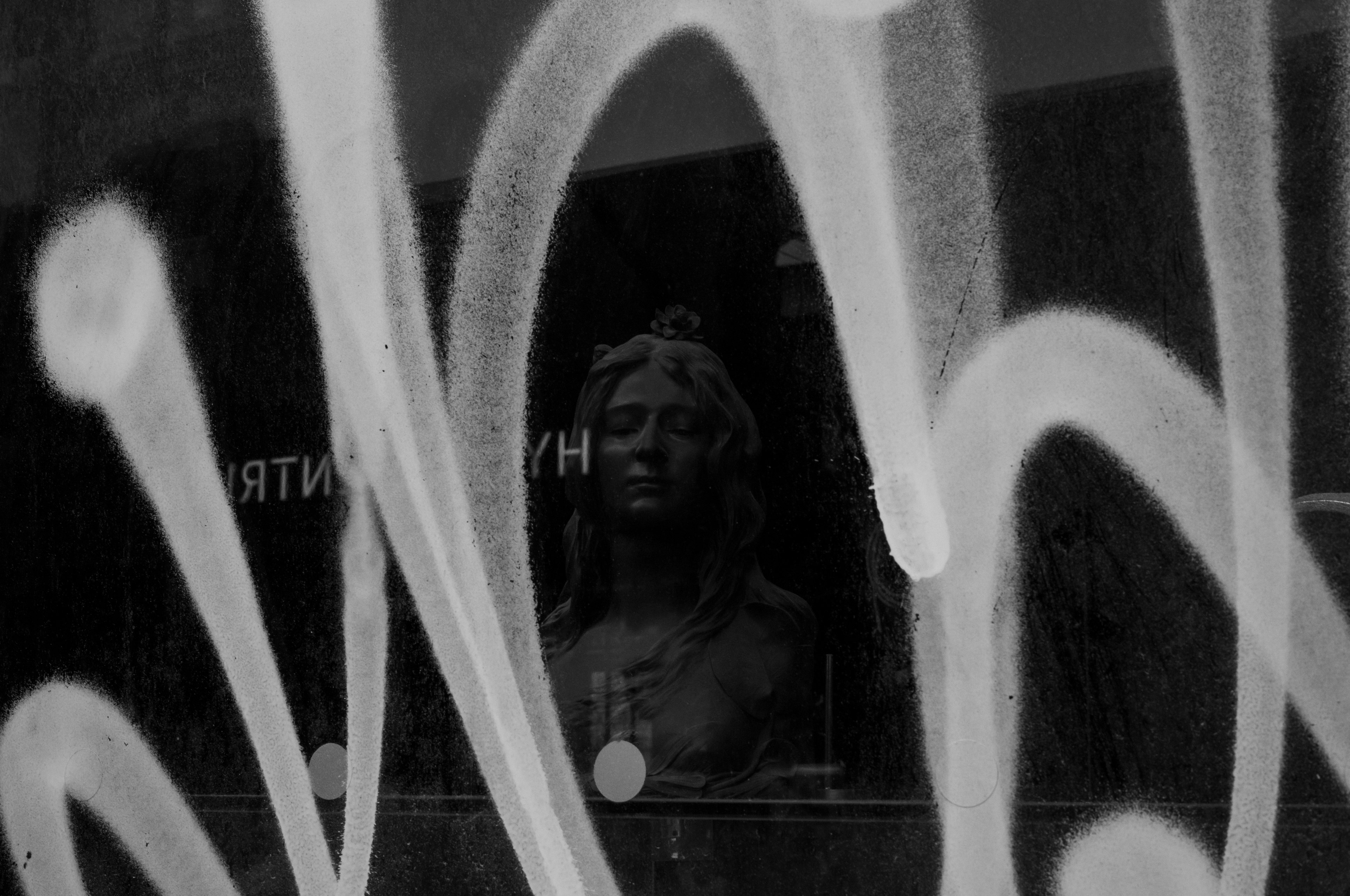 Image of a sculpture's face visible behind white graffiti