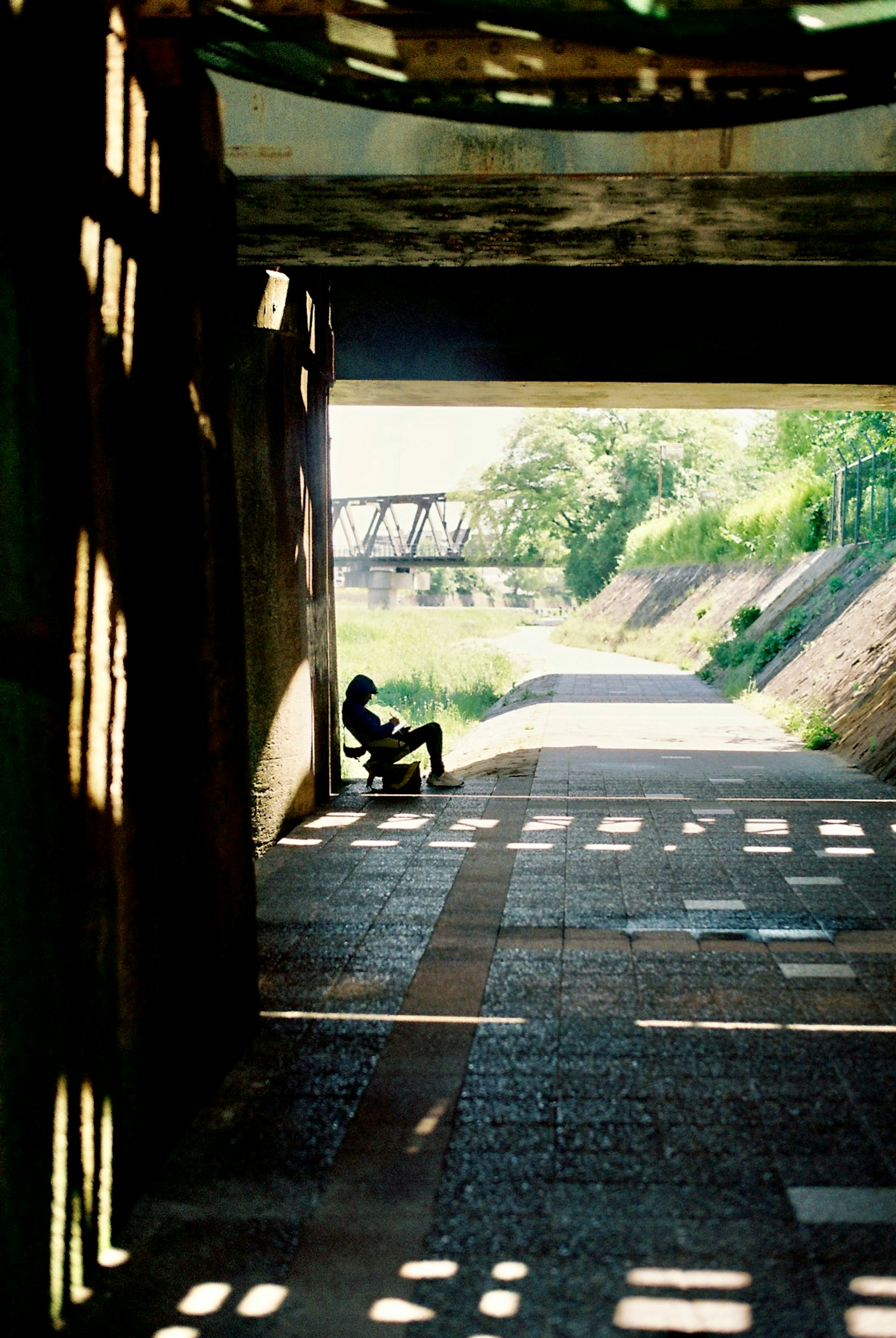 Figura in silhouette seduta in un tunnel illuminato dal sole con vista sul fiume