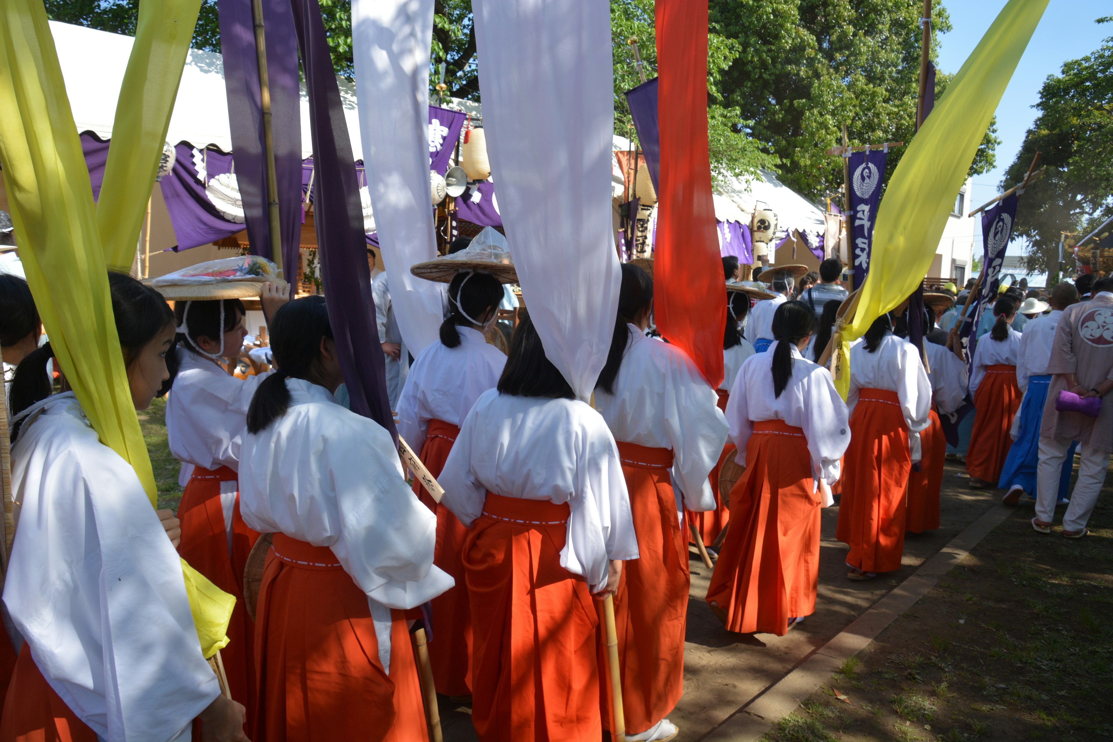 Sebuah adegan festival dengan orang-orang berpakaian tradisional memegang spanduk berwarna-warni