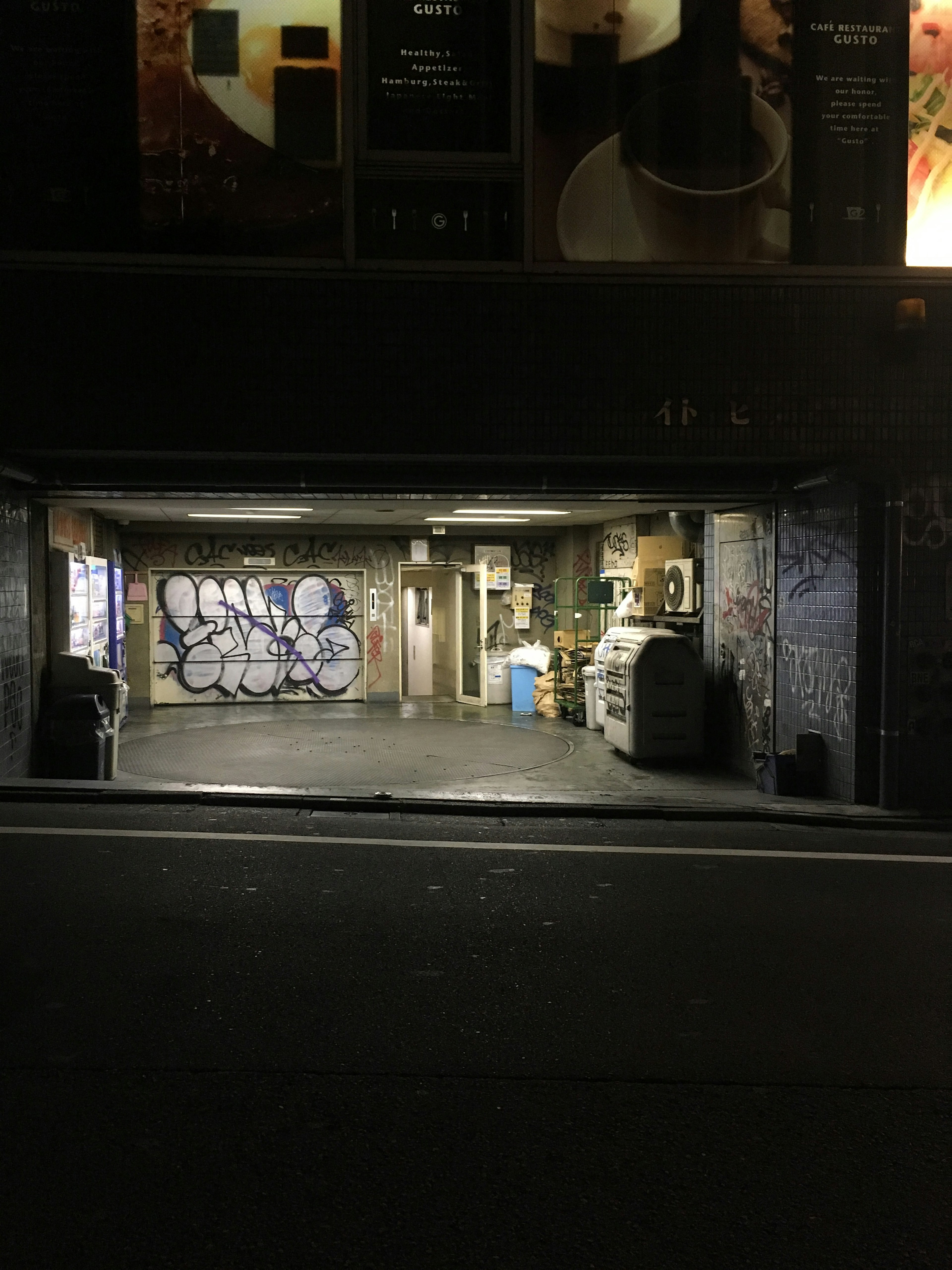 Dimly lit garage interior featuring graffiti and trash bins