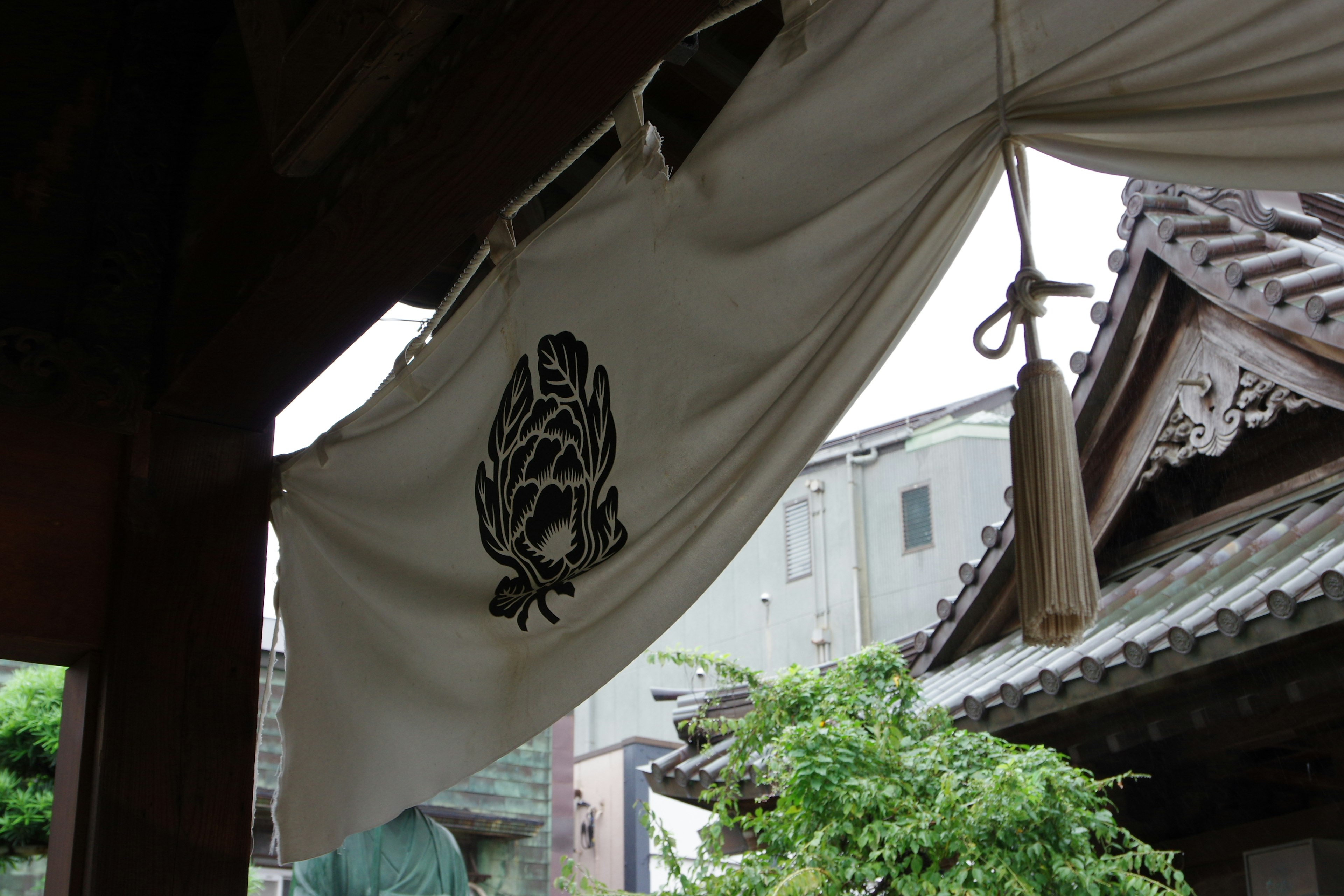 White fabric banner with embroidered emblem at the entrance of a traditional Japanese building