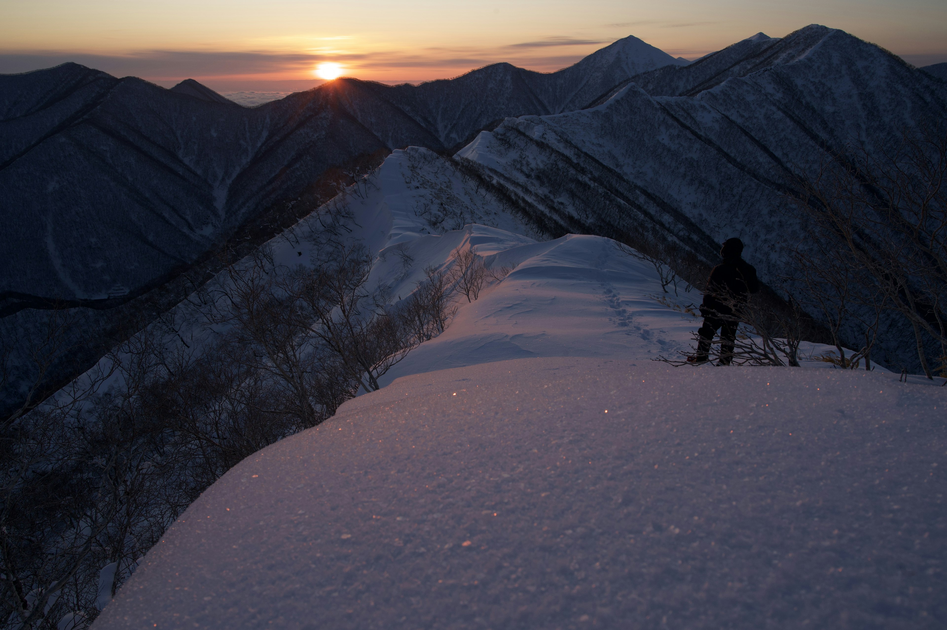 Personne debout sur une crête montagneuse enneigée au coucher du soleil