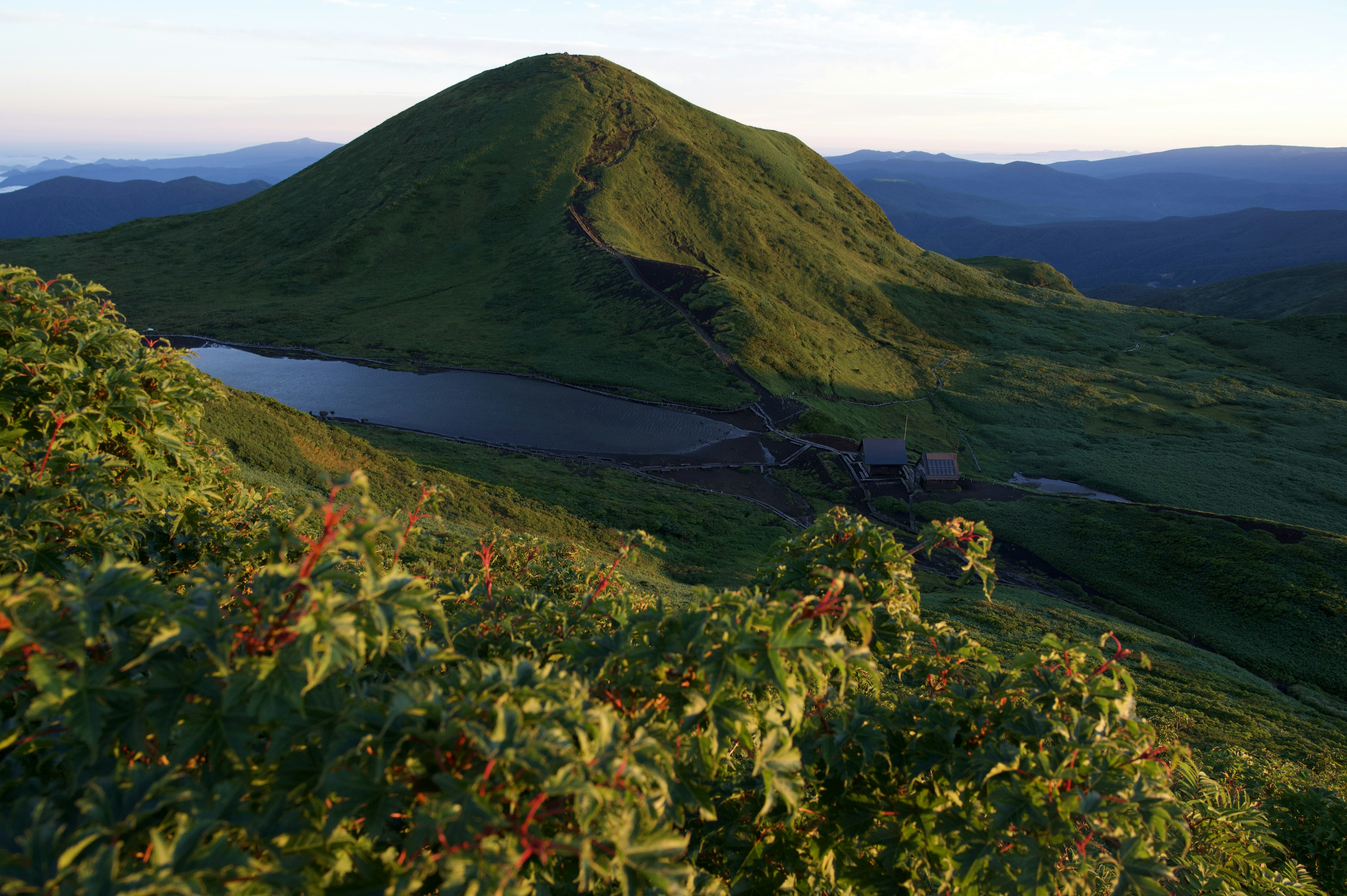 Paisaje montañoso verde con un estanque a la luz de la mañana